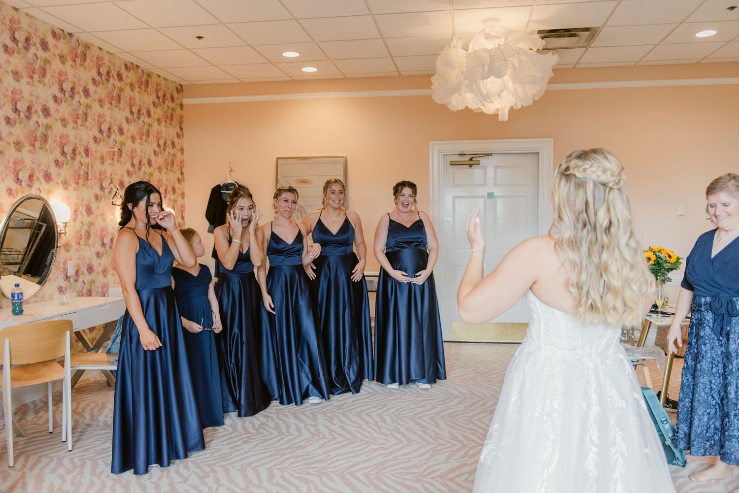 Central MN Wedding Photos | Bride in white gown reveals herself to bridesmaids in matching navy blue dresses before ceremony.