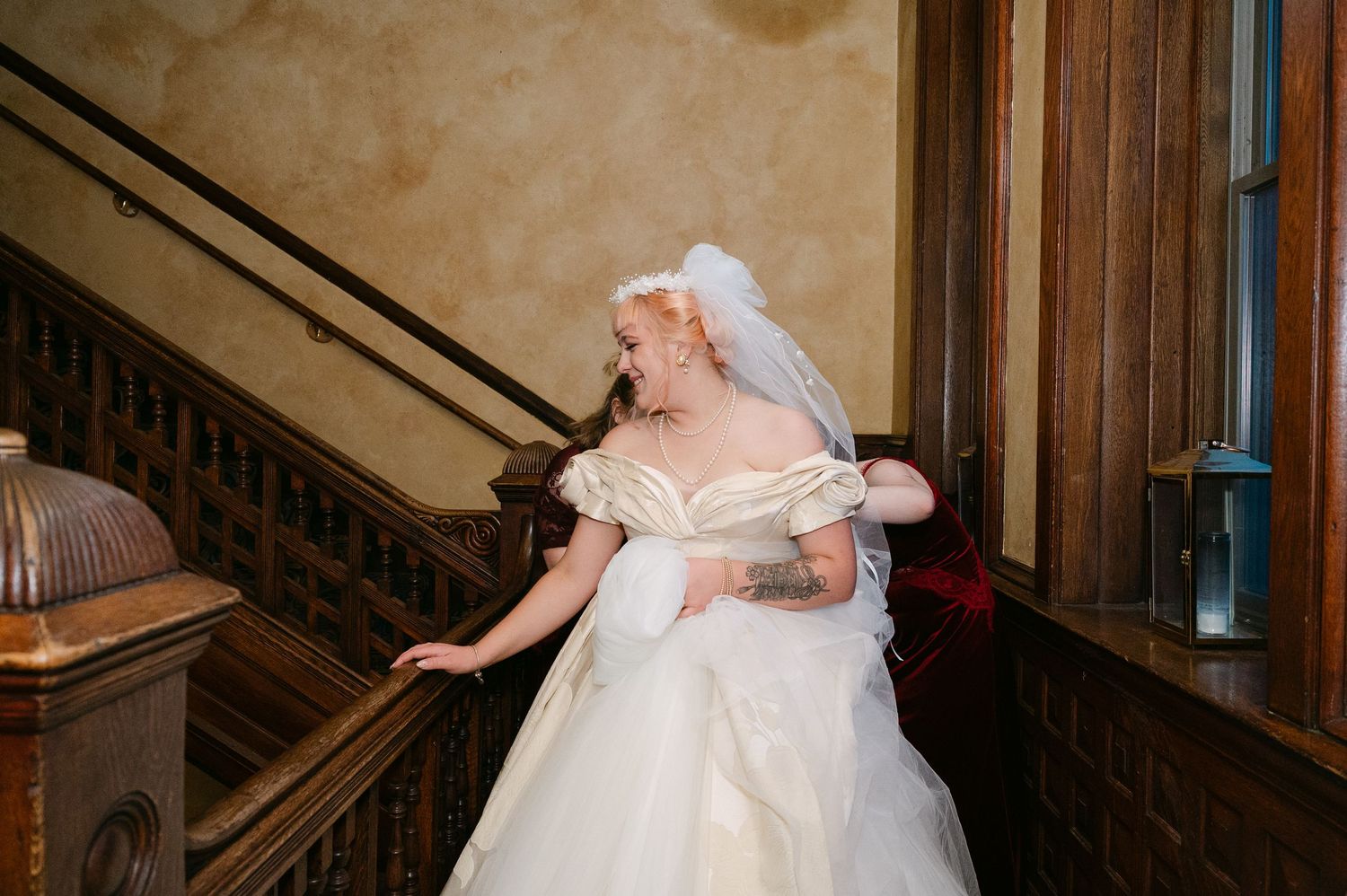 Central MN Wedding Photos | Bride in off-shoulder ball gown and veil poses gracefully on ornate wooden staircase.