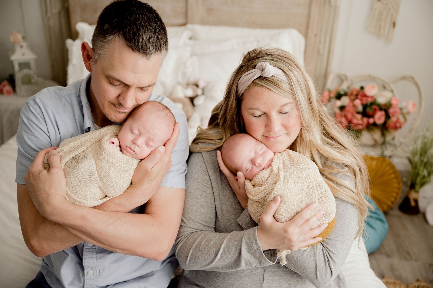 Parents tenderly holding their swaddled newborn twins in a cozy decorated nursery.
