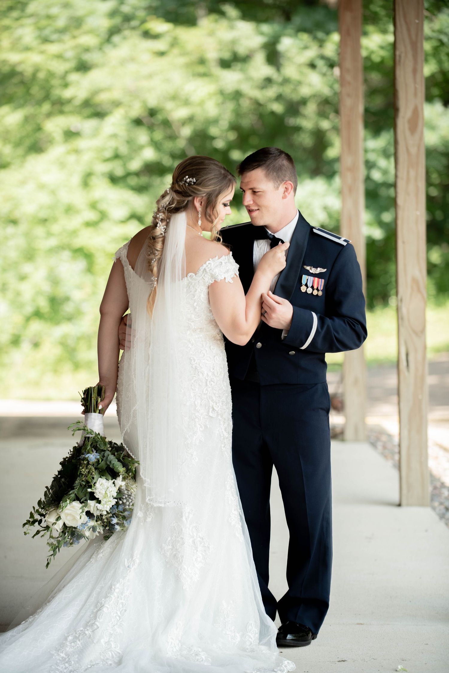 A romantic wedding moment outdoors showing a military dress uniform and elegant white bridal gown with bouquet.