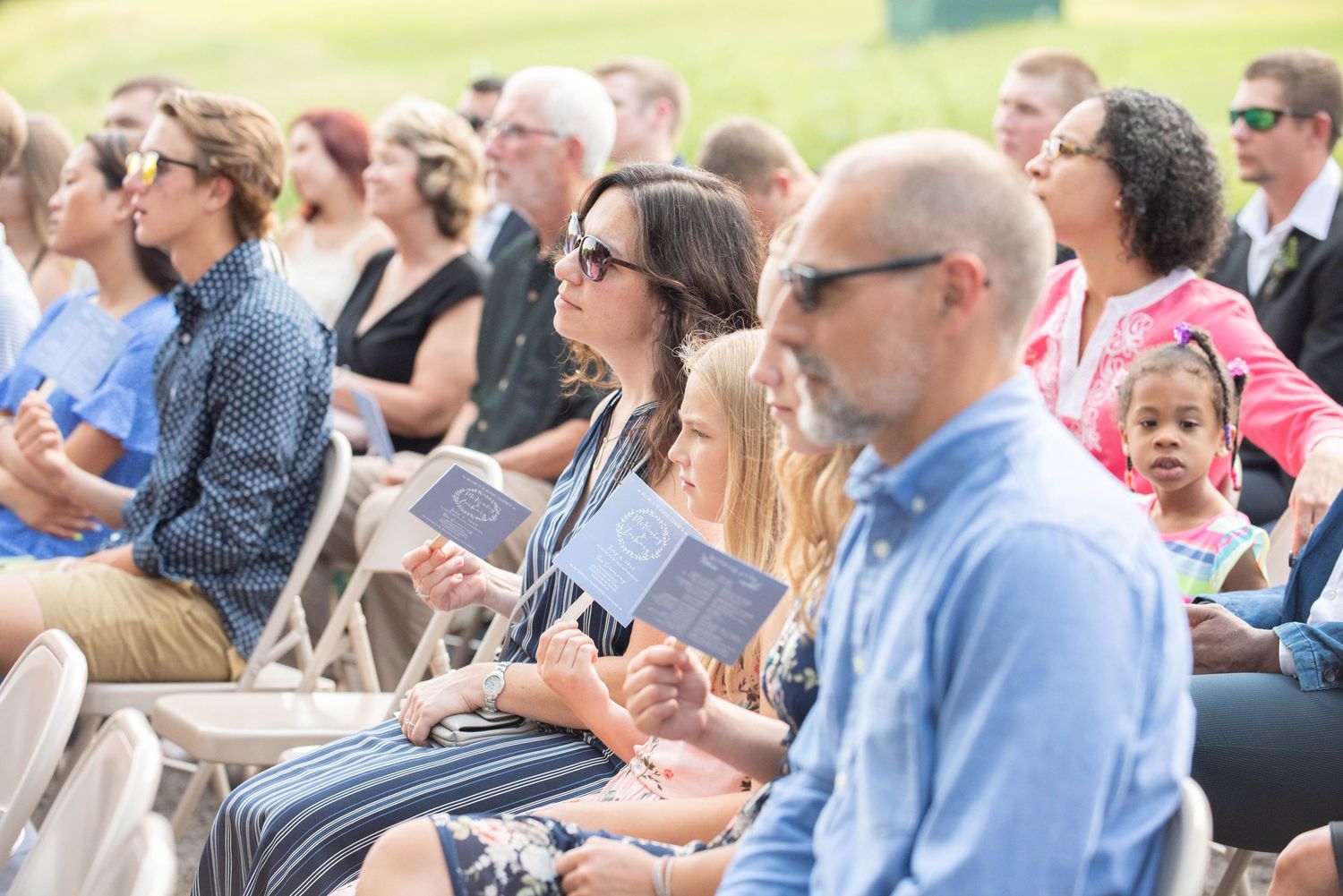 Wedding guests stand and applaud during an outdoor ceremony amongst green trees and white decor. Zimmerman MN Weddings