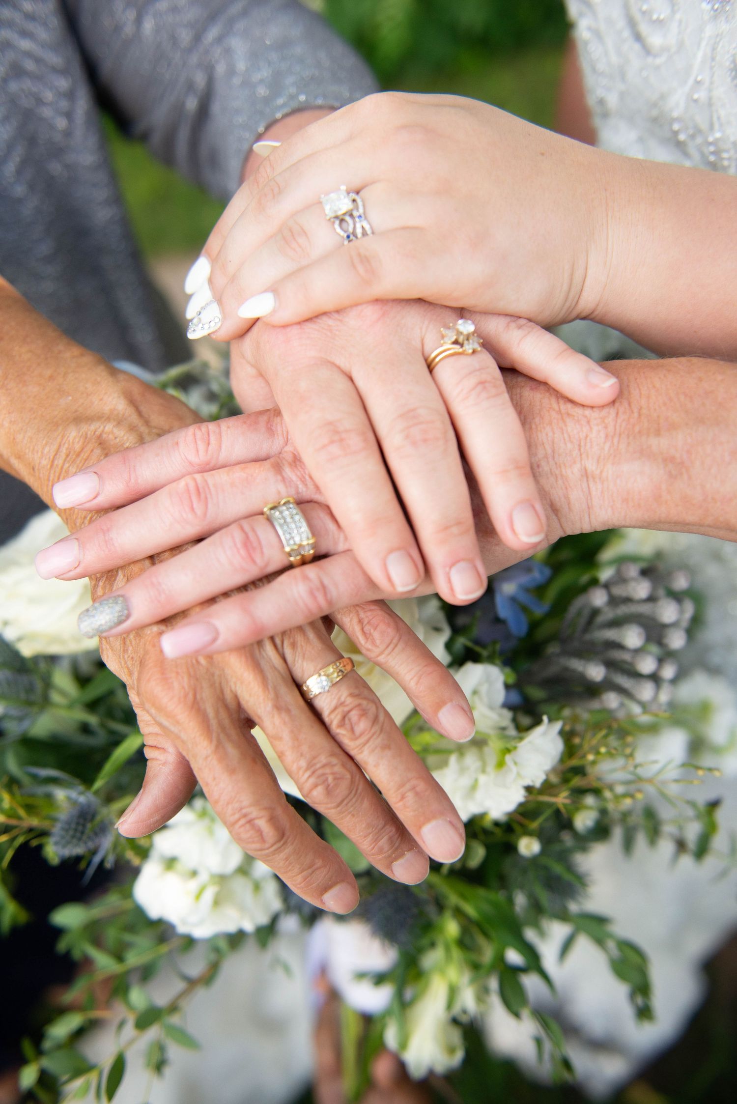 Close-up of wedding rings and hands stacked together over a white floral bouquet. Zimmerman MN Weddings