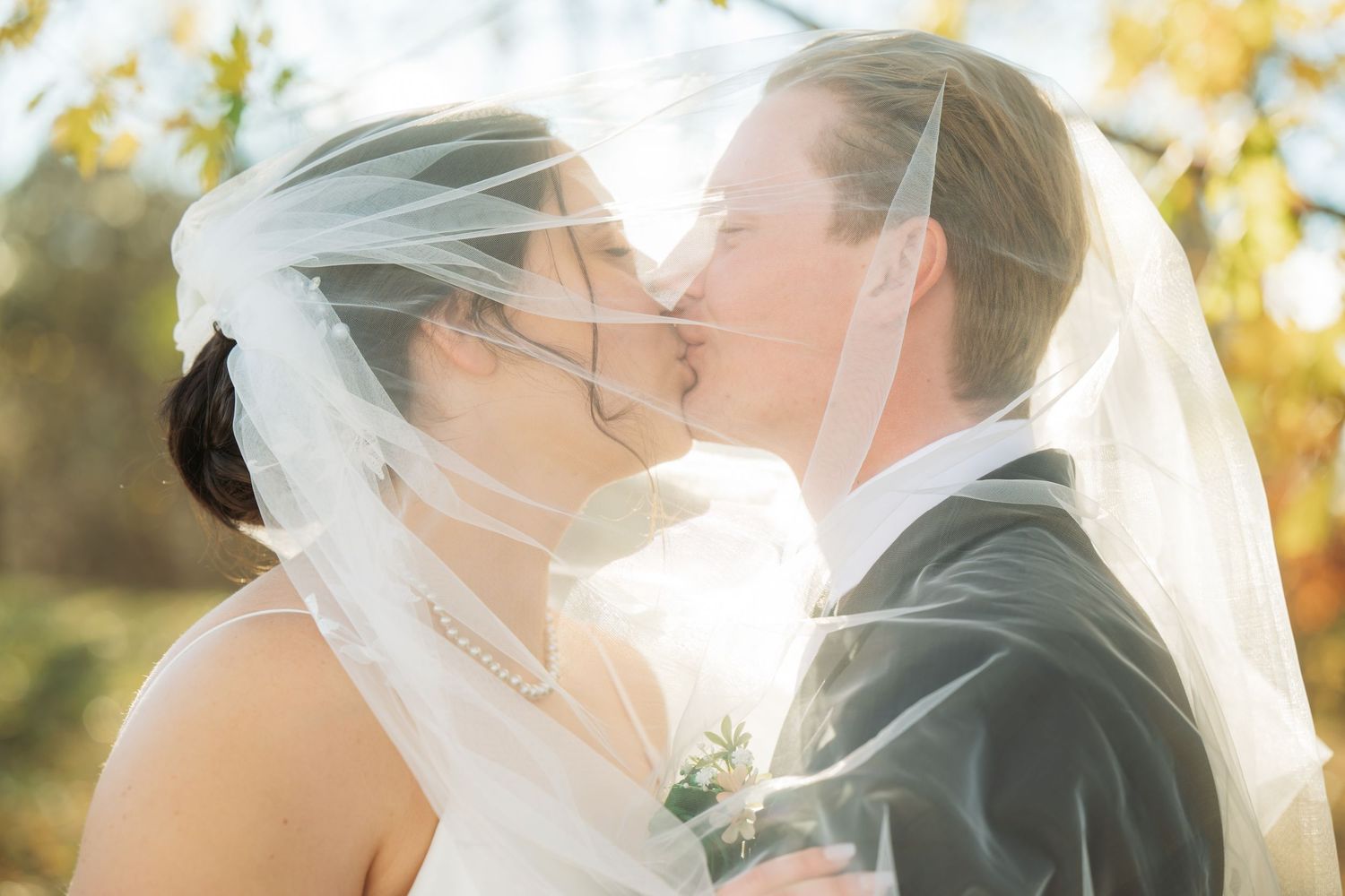 Romantic wedding couple sharing intimate moments under golden sunlight and flowing veil.