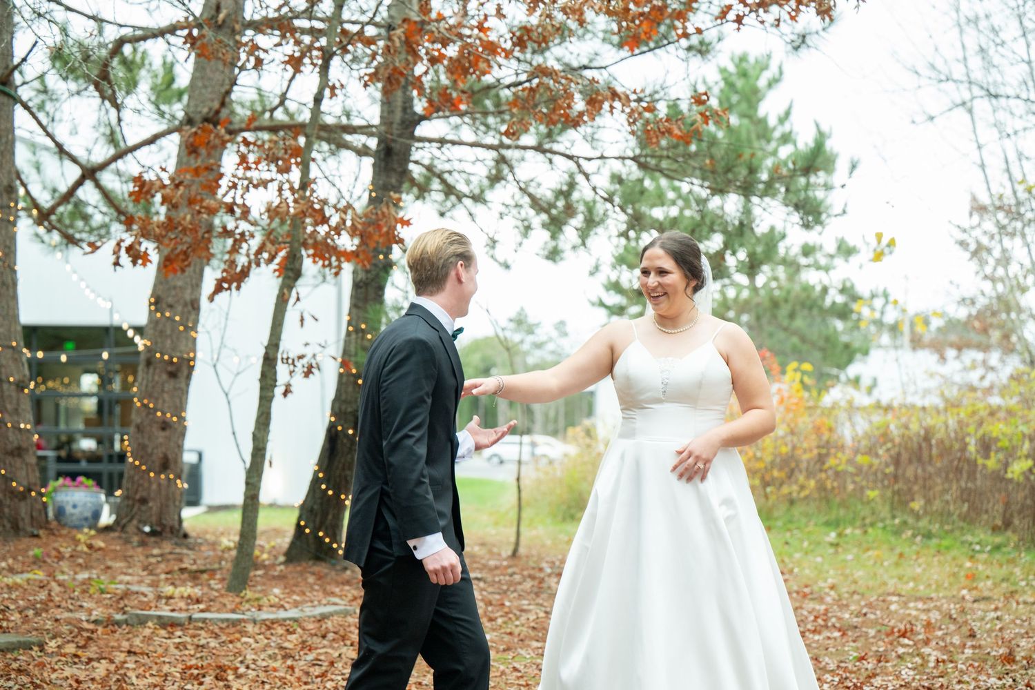A couple shares a romantic moment during their autumn wedding ceremony surrounded by fallen leaves in a wooded setting.