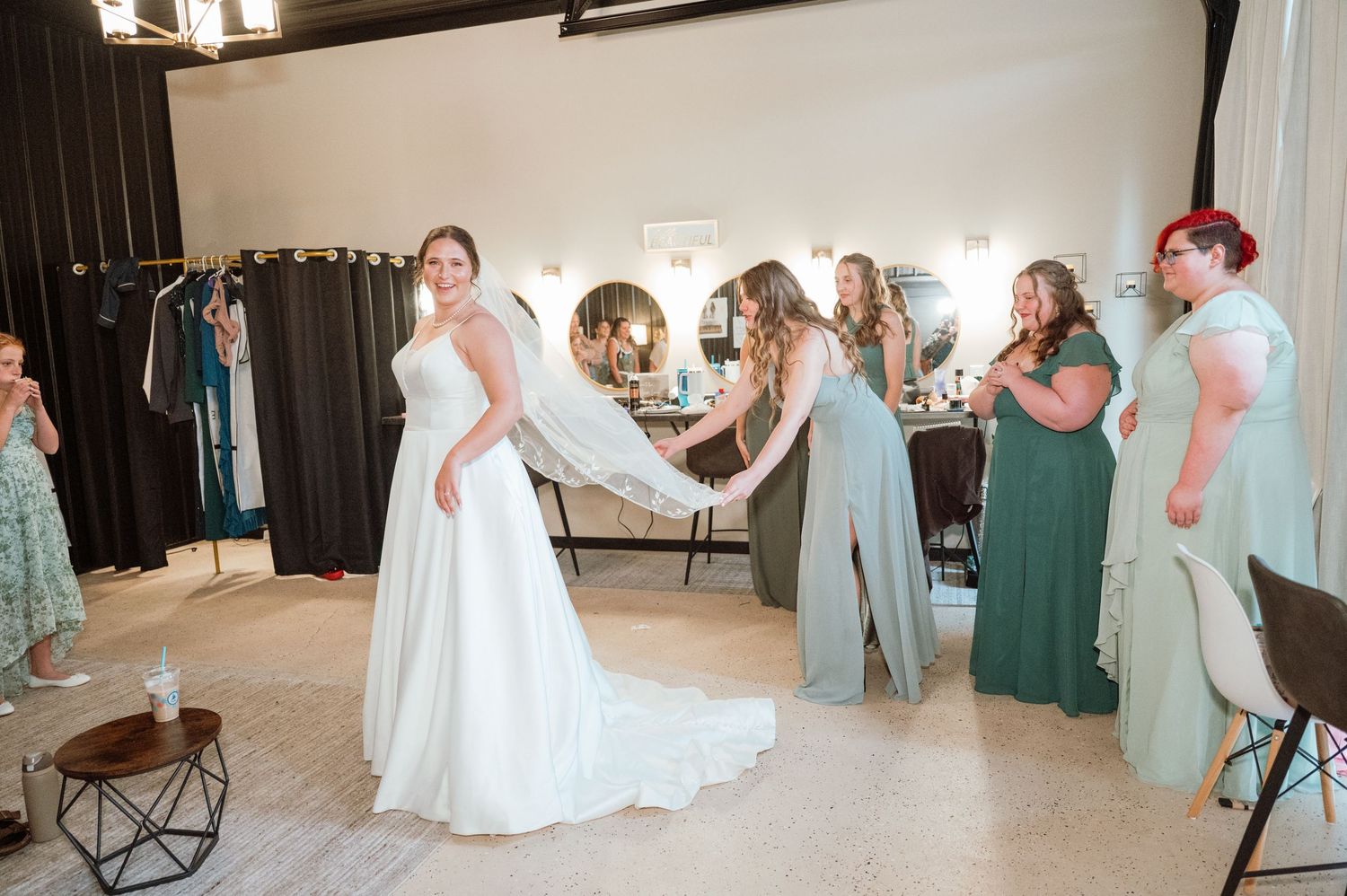 Wedding party members in green dresses react with excitement and joy during a first look reveal moment.