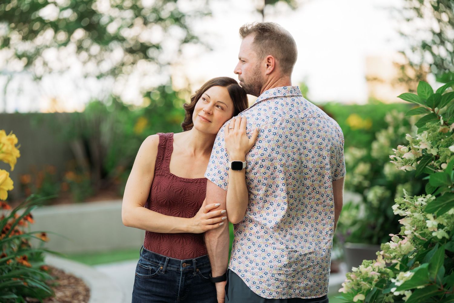 A couple shares a tender moment together in a lush garden setting with blooming flowers and greenery.