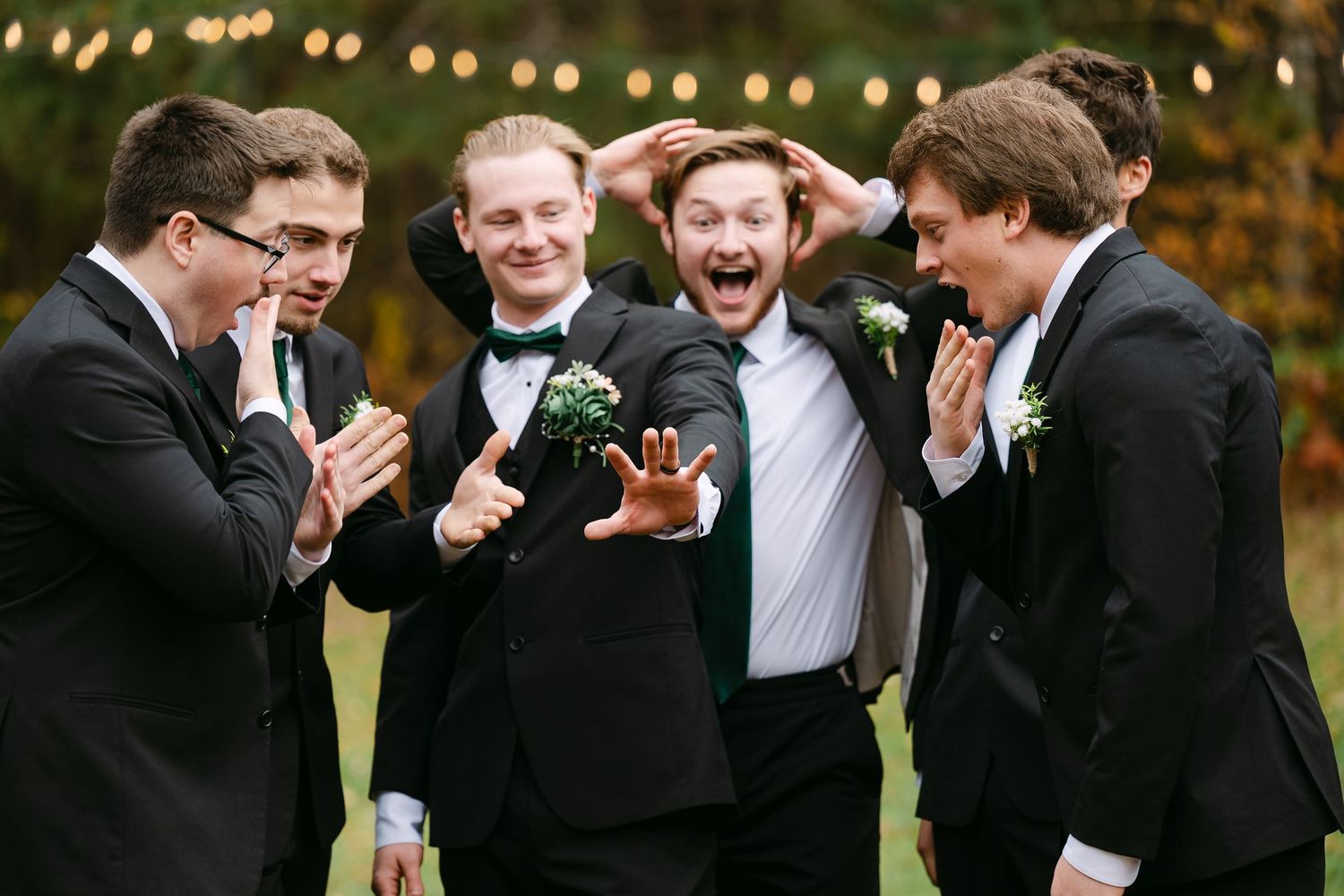 Groomsmen in black tuxedos laughing and celebrating outdoors.