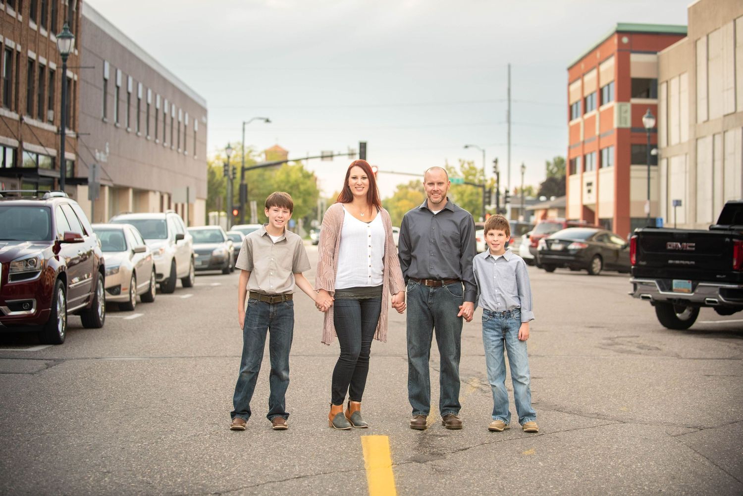 A group of people walking on a city street with parked cars and buildings visible in the background.
