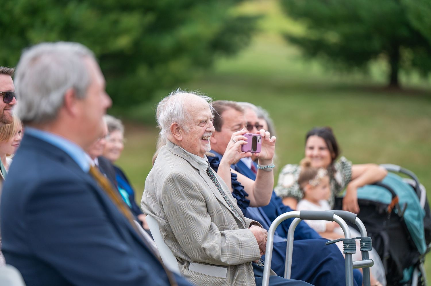 Wedding attendees watch the ceremony from their seats in an outdoor garden setting.