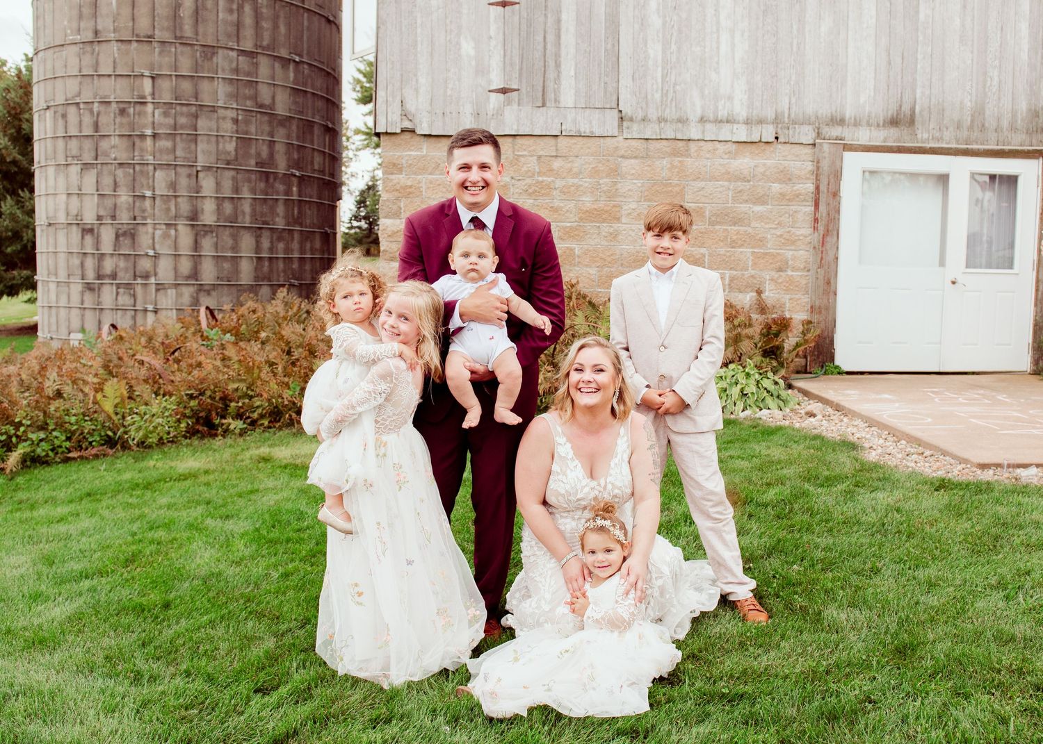 Wedding party gathers for formal portraits in front of rustic stone building.