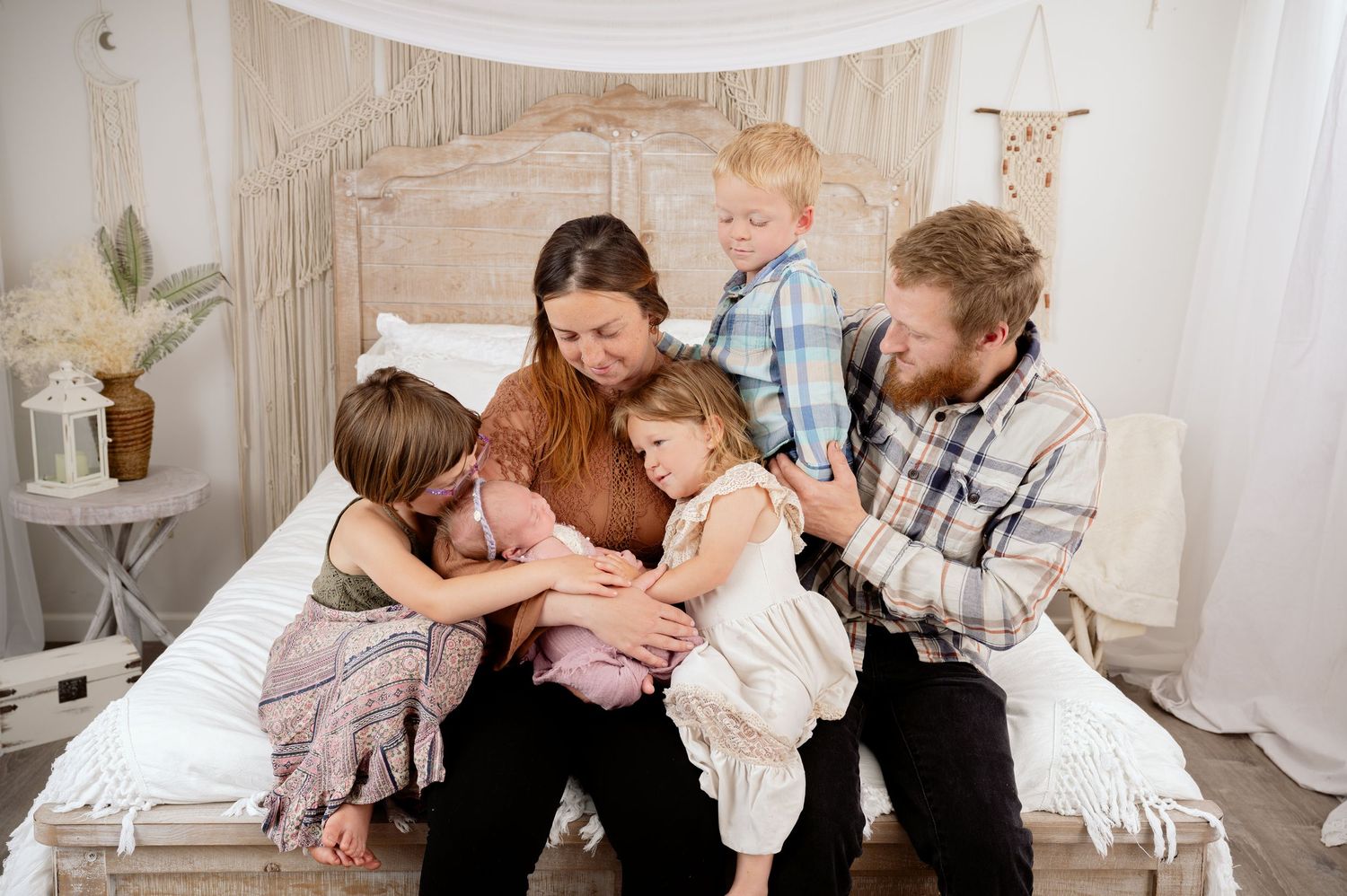 Candid family moment with parents and children sharing laughs while sitting on a white bed in a cozy bedroom.