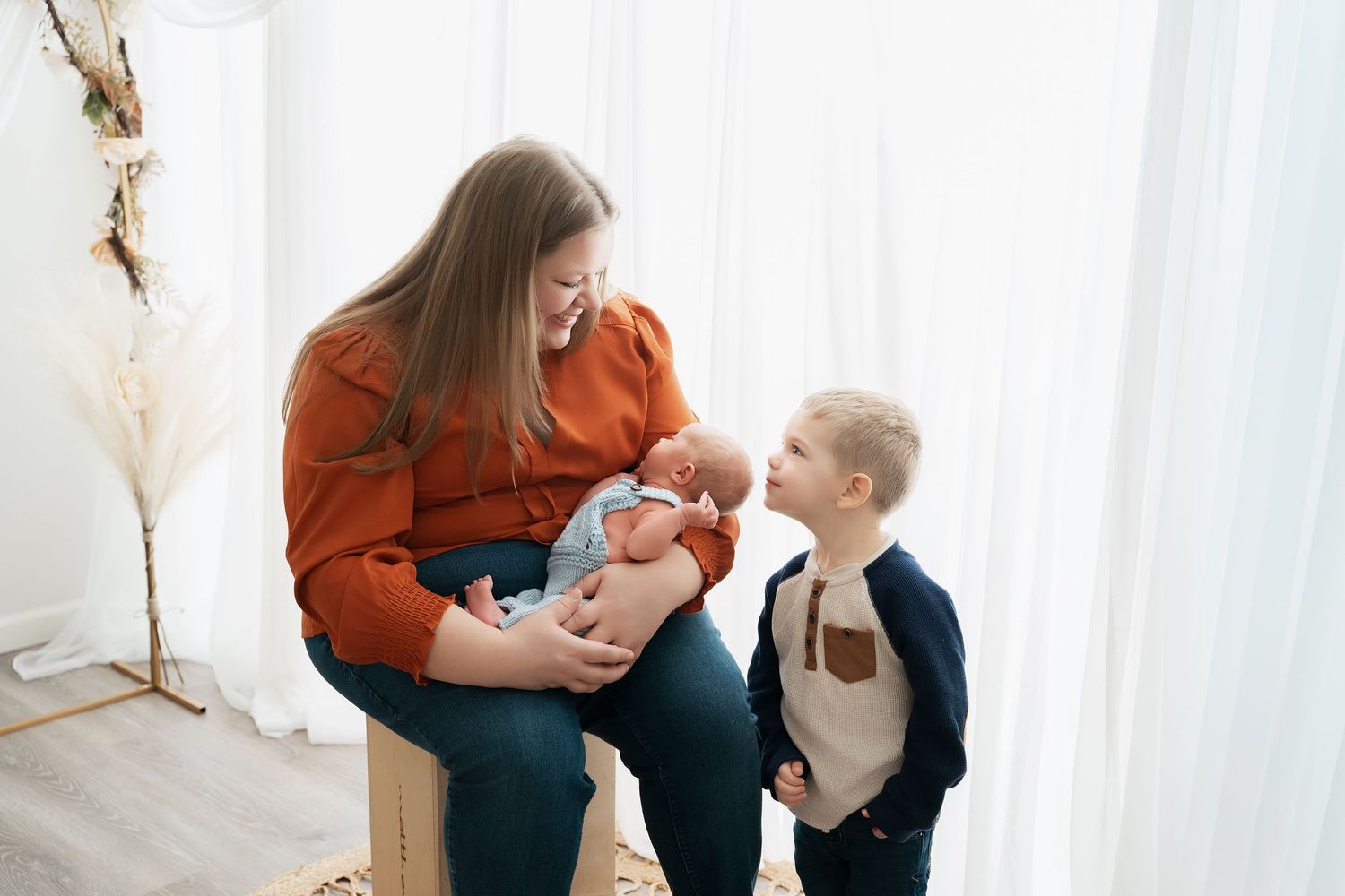 Minnesota Best newborn photographer a parent and baby share tender moments in a bright white studio setting wearing orange and blue outfits.