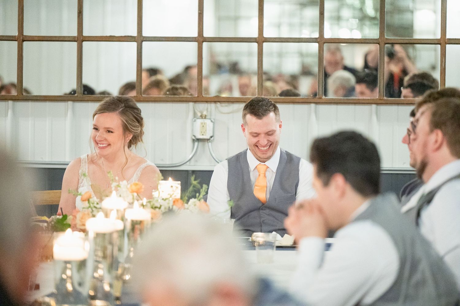 Bride and groom laugh together at the head table during their wedding reception.