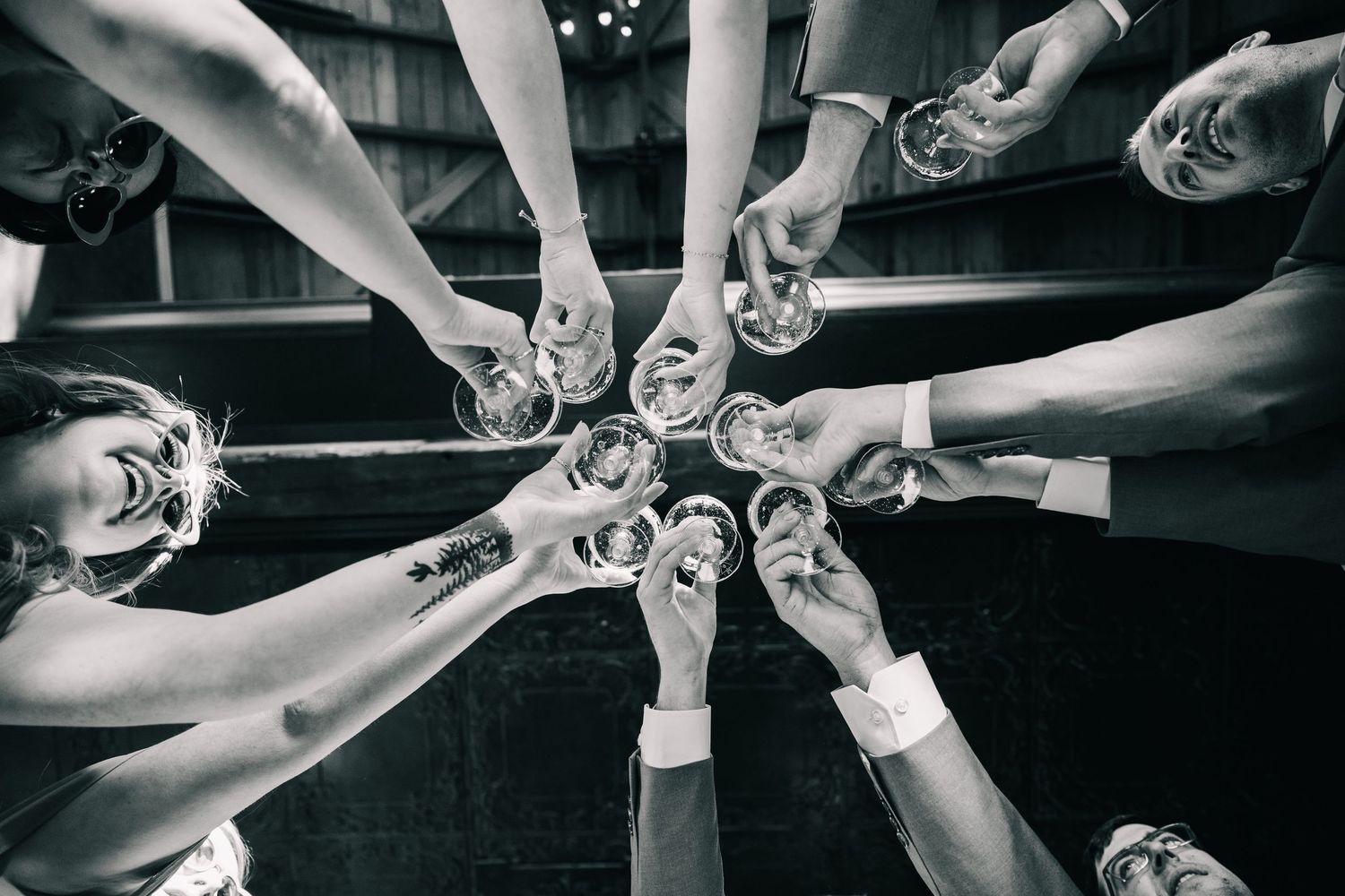 Black and white overhead shot of wedding guests toasting with glasses in a circle.