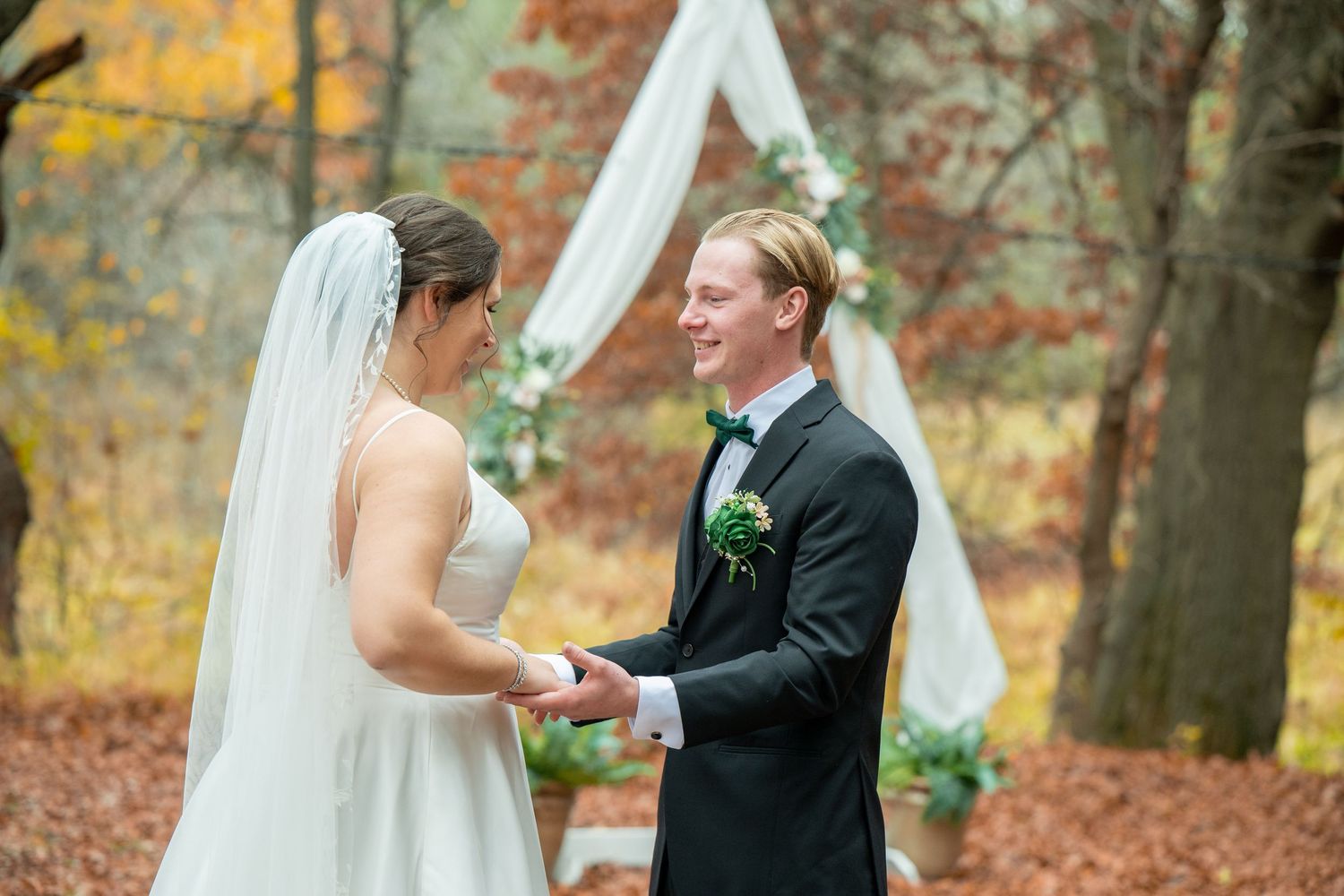 A couple shares a romantic moment during their autumn wedding ceremony surrounded by colorful fall foliage.