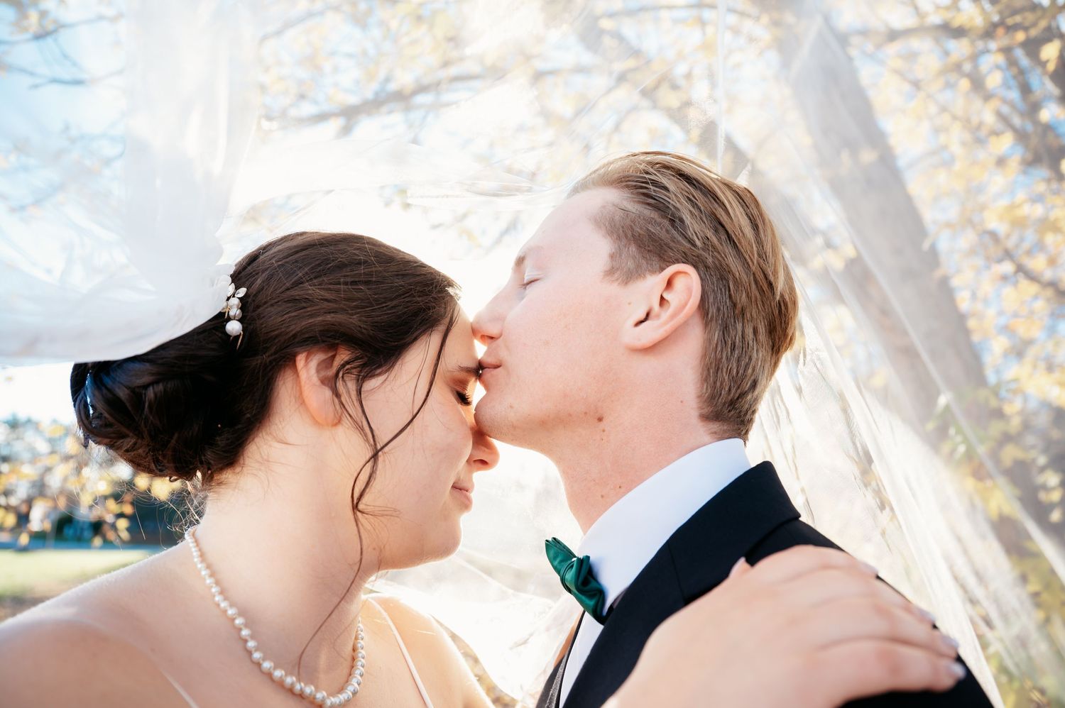 Romantic wedding couple sharing intimate moments against a bright outdoor backdrop.