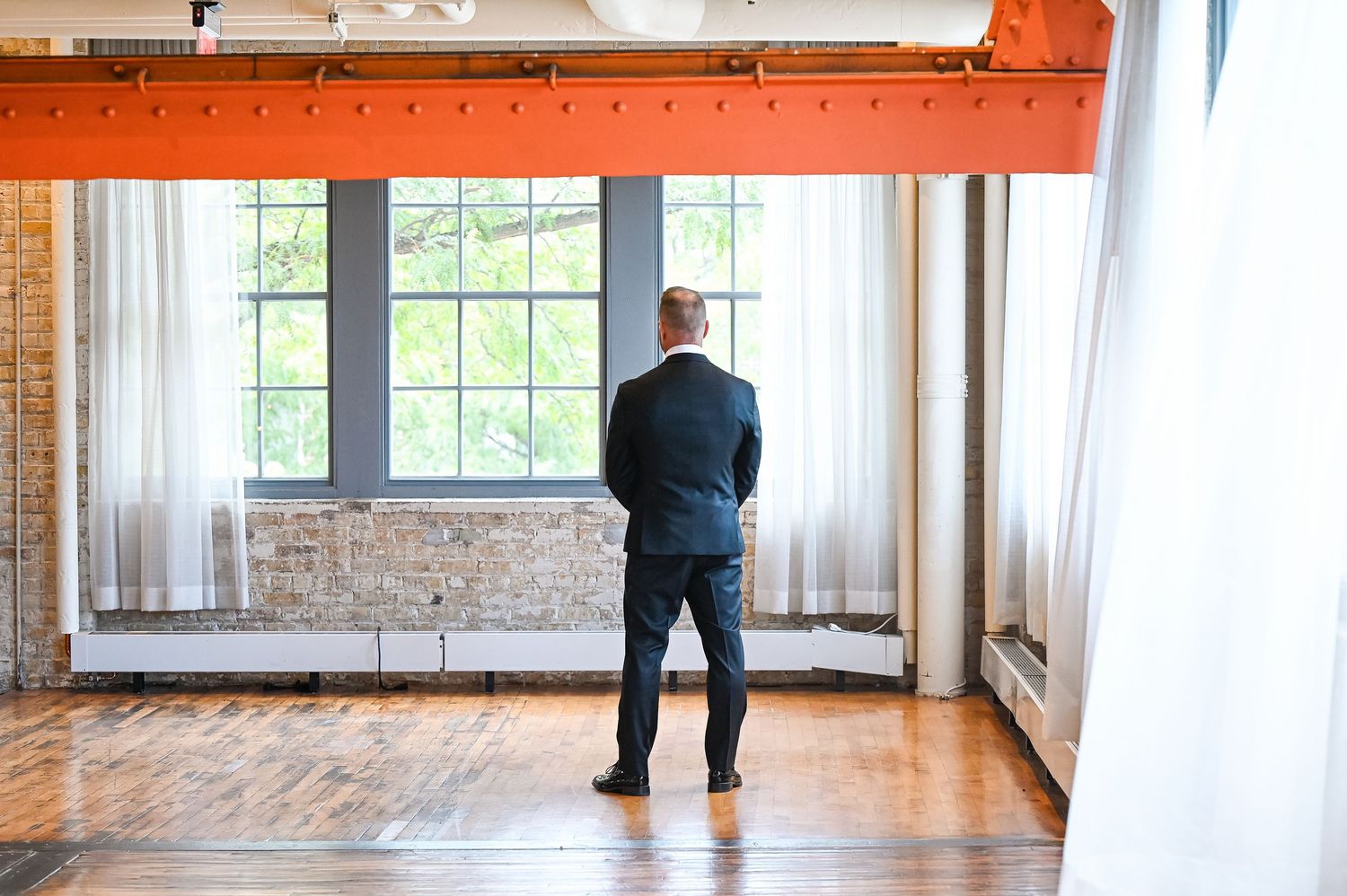 An elegant room features exposed brick walls, large windows, and flowing white curtains.