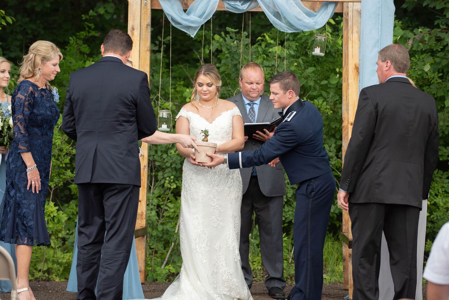 Wedding party members gather beneath a rustic wooden arch during an outdoor garden ceremony. Zimmerman MN Weddings