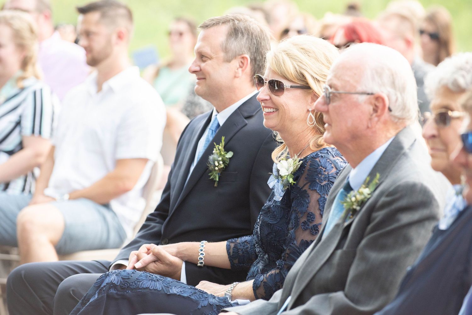 Wedding guests sit in white chairs at an outdoor ceremony surrounded by greenery and natural scenery. Zimmerman MN Weddings