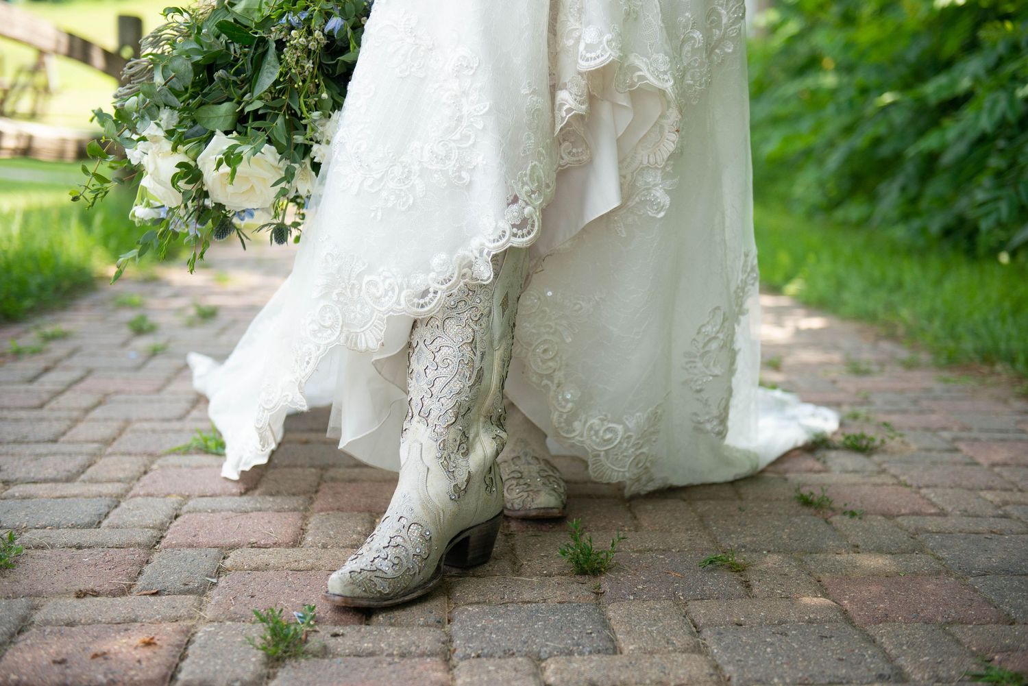 Close-up of white lace wedding dress detail on brick pathway. Zimmerman MN Weddings