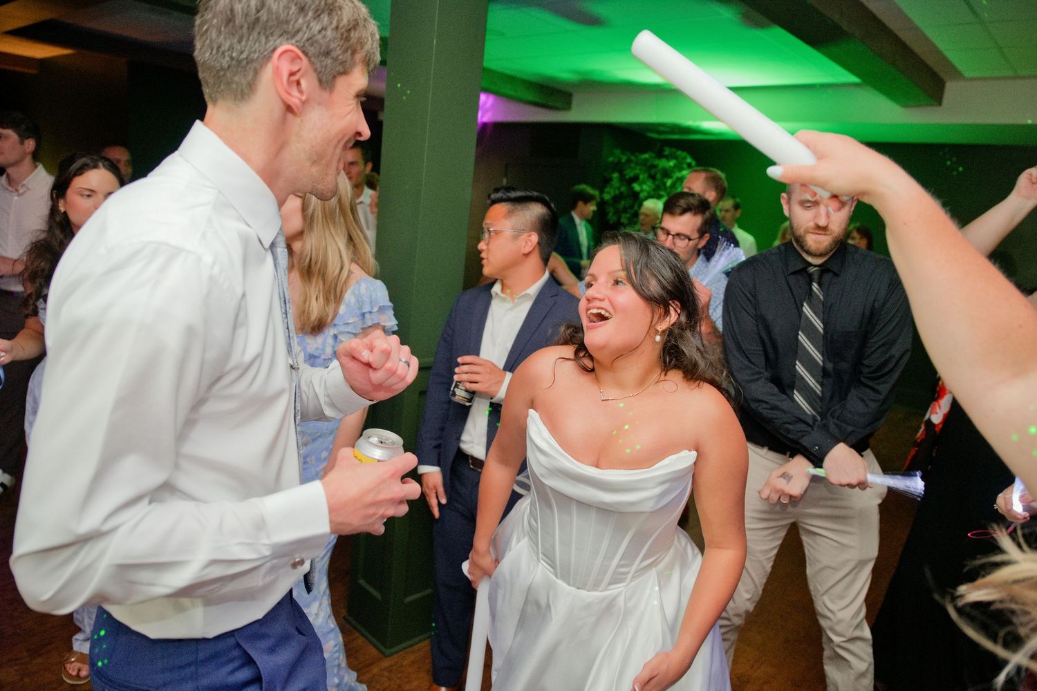 Bride in white strapless gown laughing joyfully with guests dancing at a lively wedding reception party.