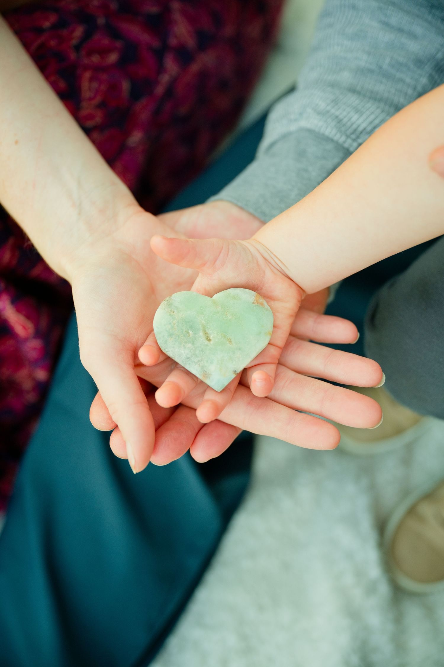 Two hands holding a green heart-shaped stone together, symbolizing love and connection.