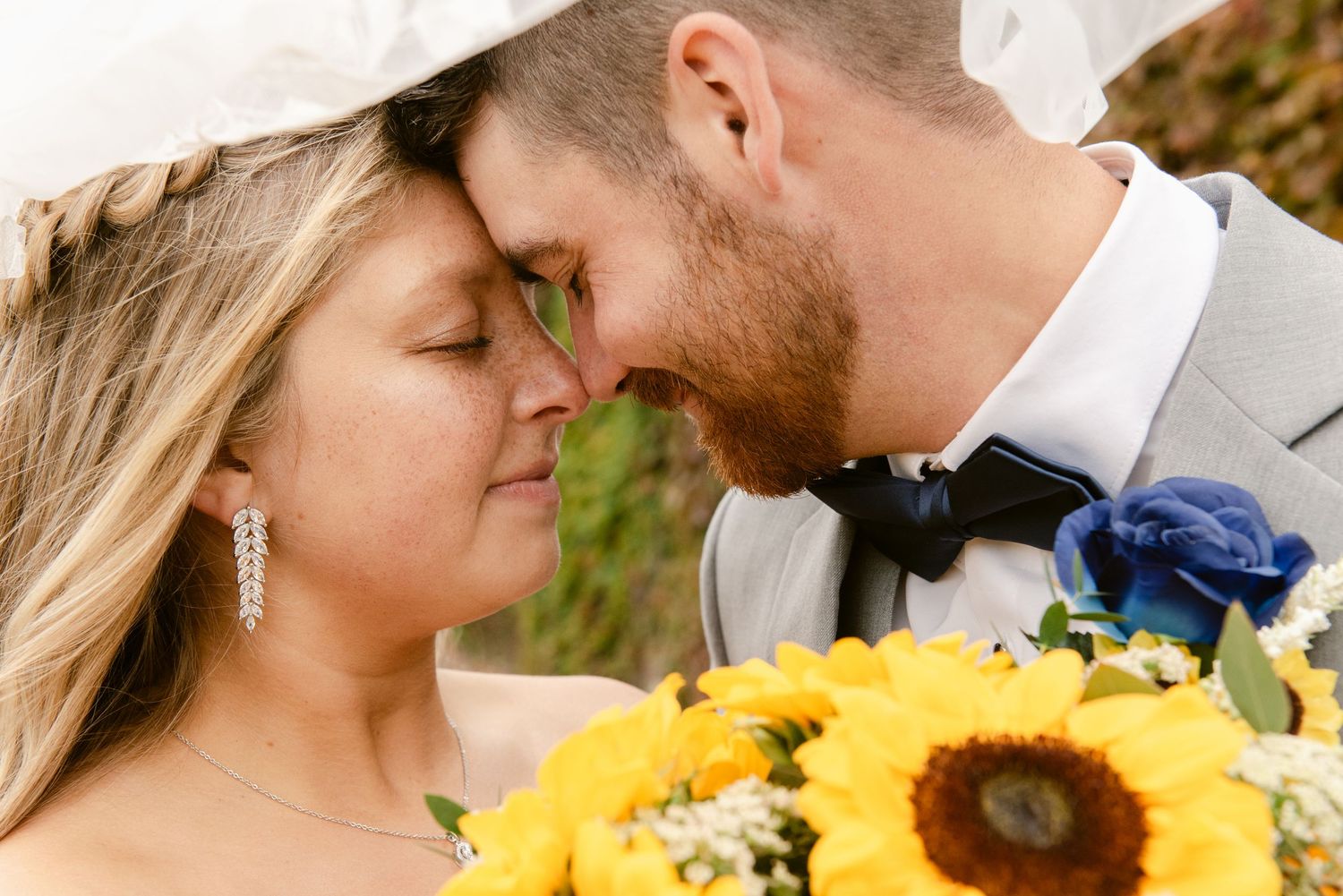 Central MN Wedding Photos | Bride and groom touching foreheads romantically with bride holding vibrant sunflower bouquet.