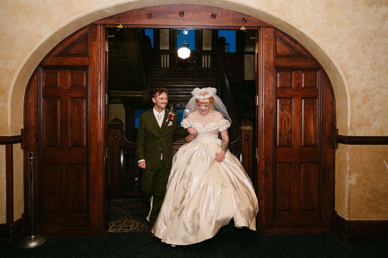 Central MN Wedding Photos | Newlyweds making grand entrance through large wooden arched doors at elegant wedding venue.