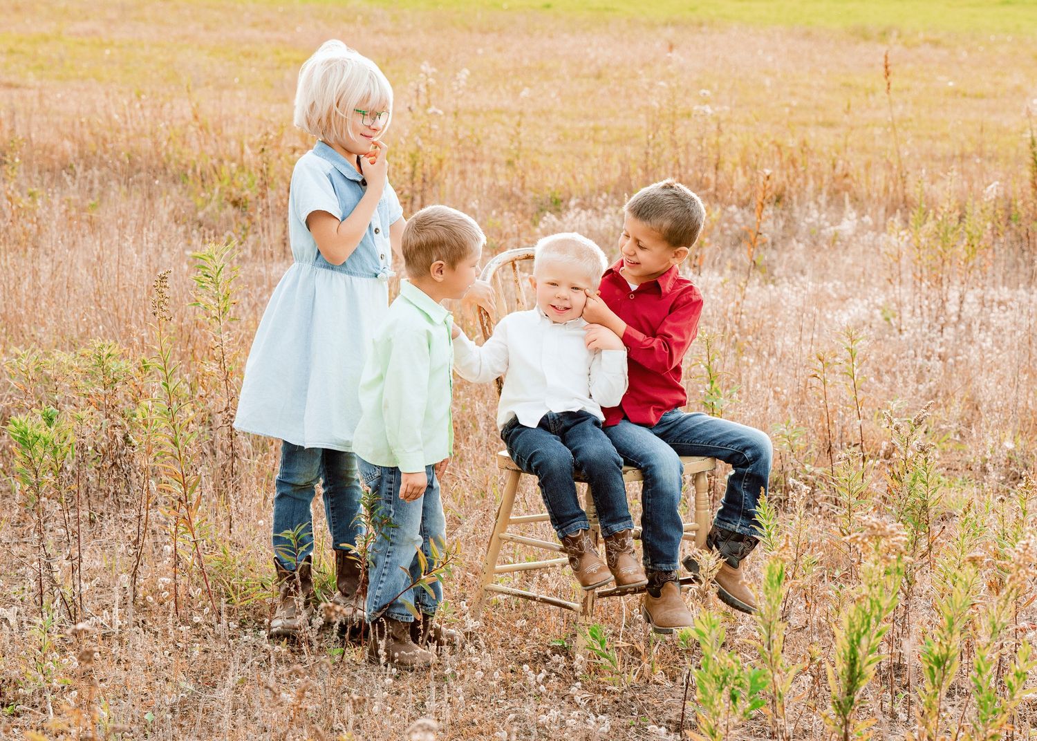 Children sit together on a log in a rustic autumn field setting.