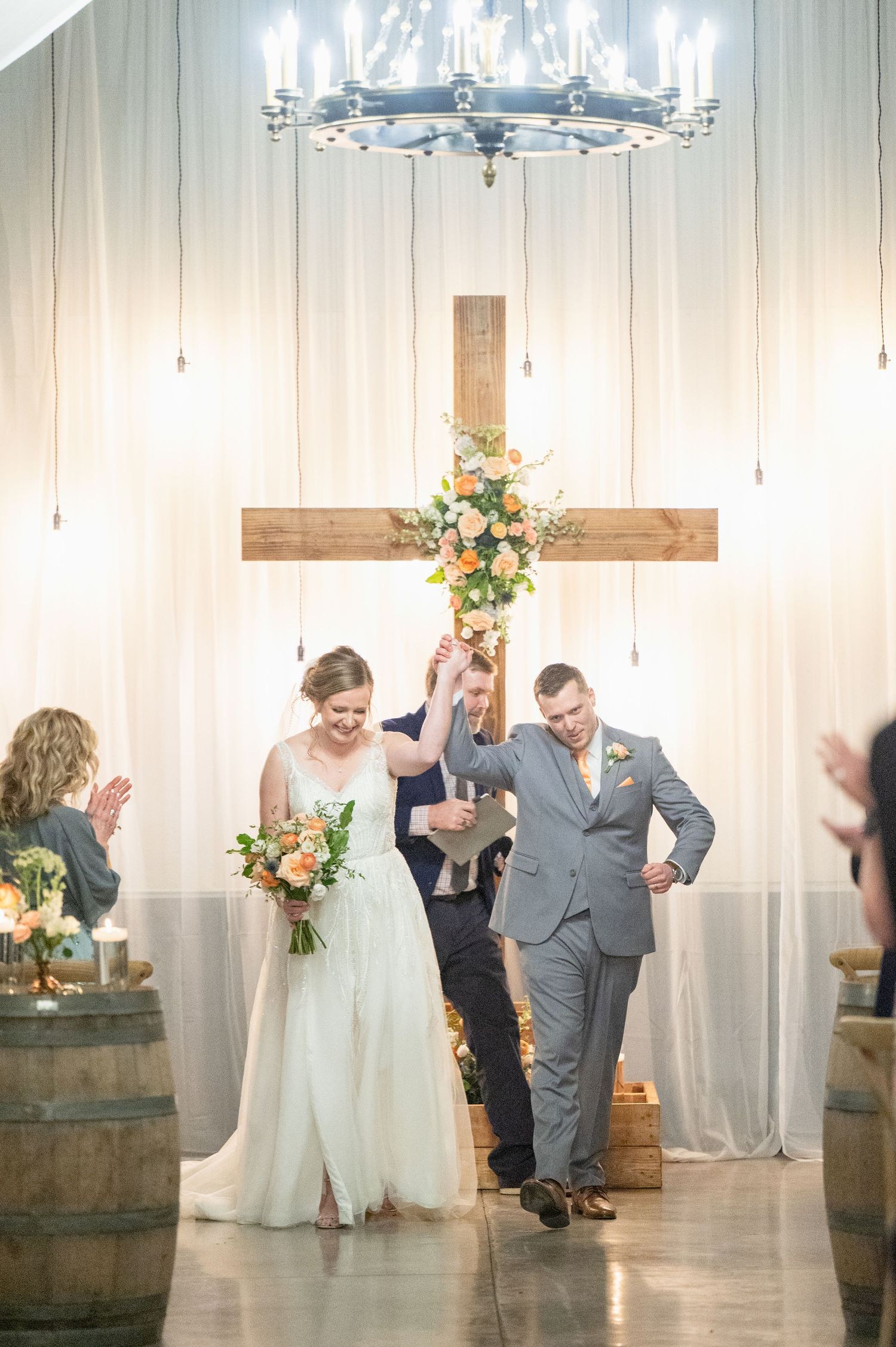 Bride and groom walk down the aisle after wedding ceremony in front of wooden cross with floral arrangement.