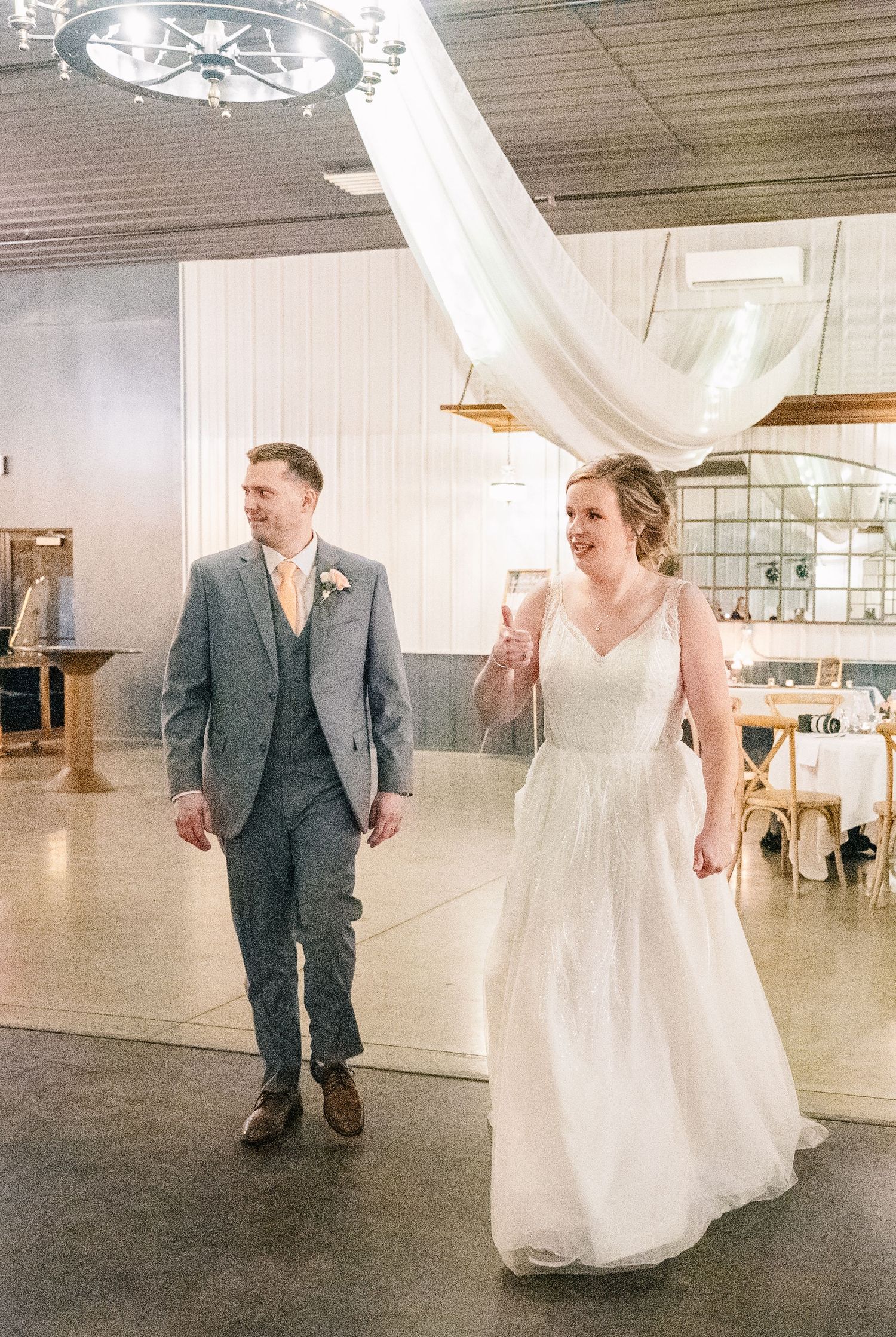 Bride in white gown and groom in gray suit entering wedding reception hall together.