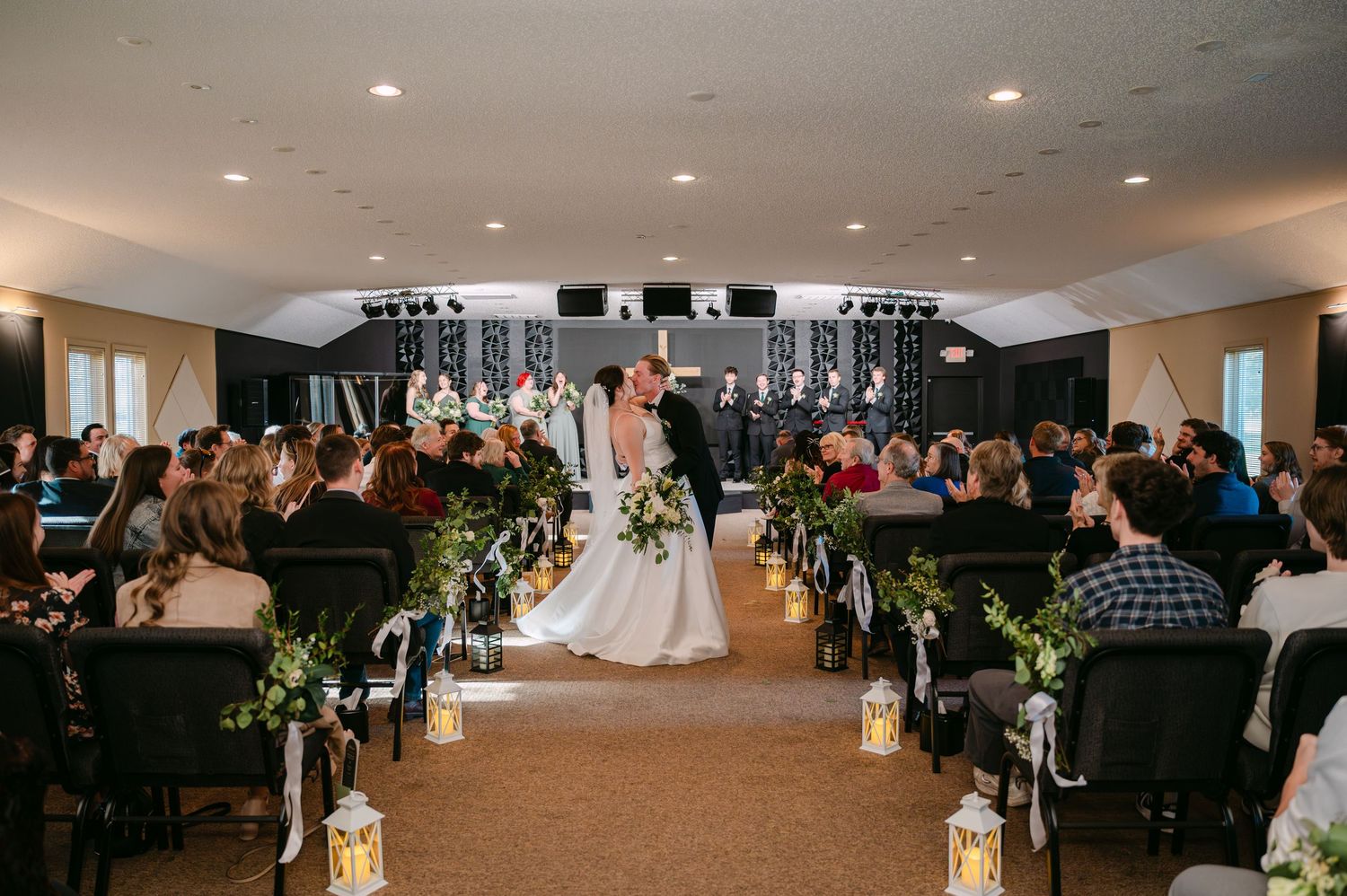 A wedding ceremony venue with white chairs and floral decorations set up in rows under soft indoor lighting.