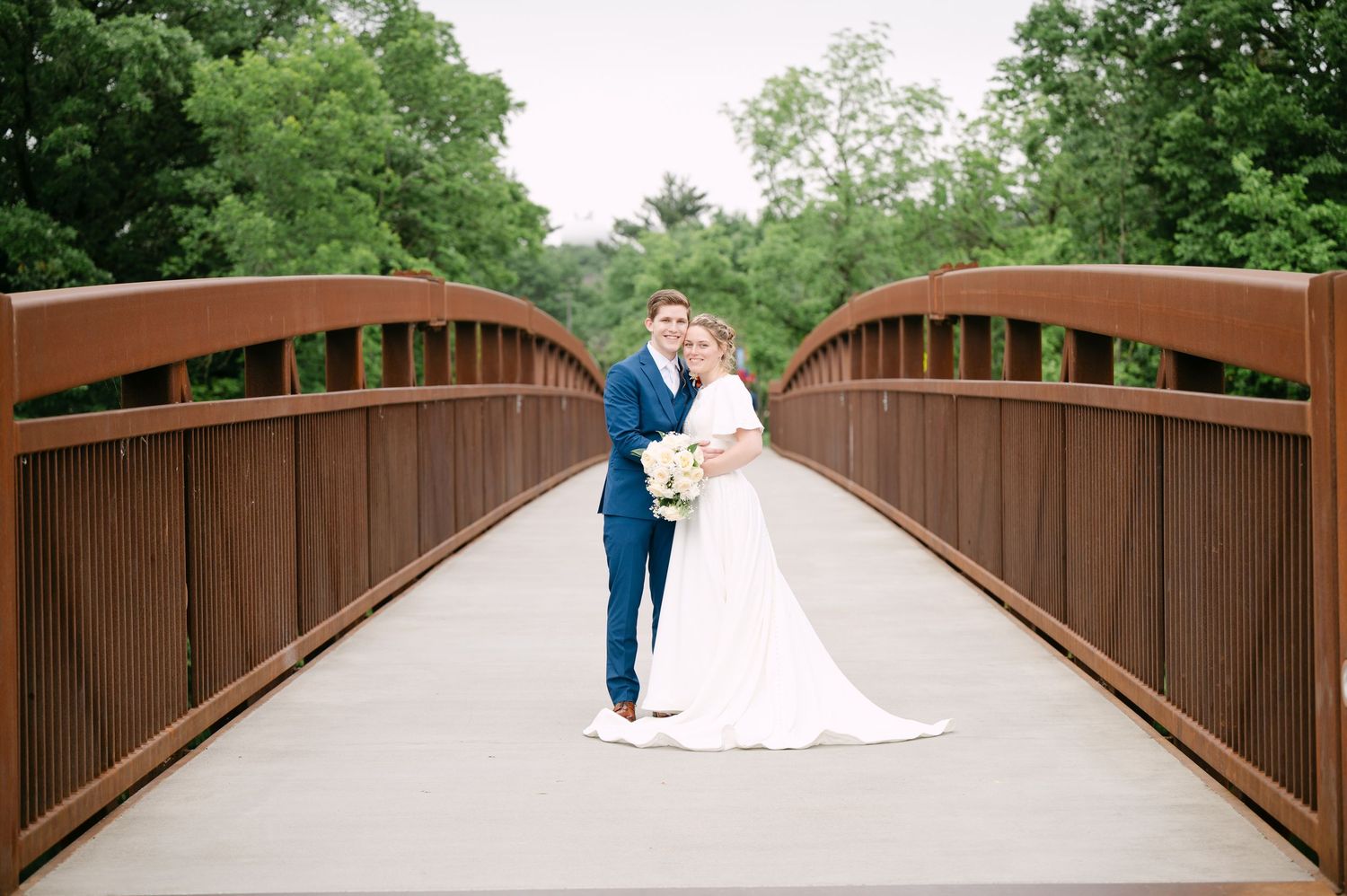 Wedding party poses on a rustic wooden bridge surrounded by trees.