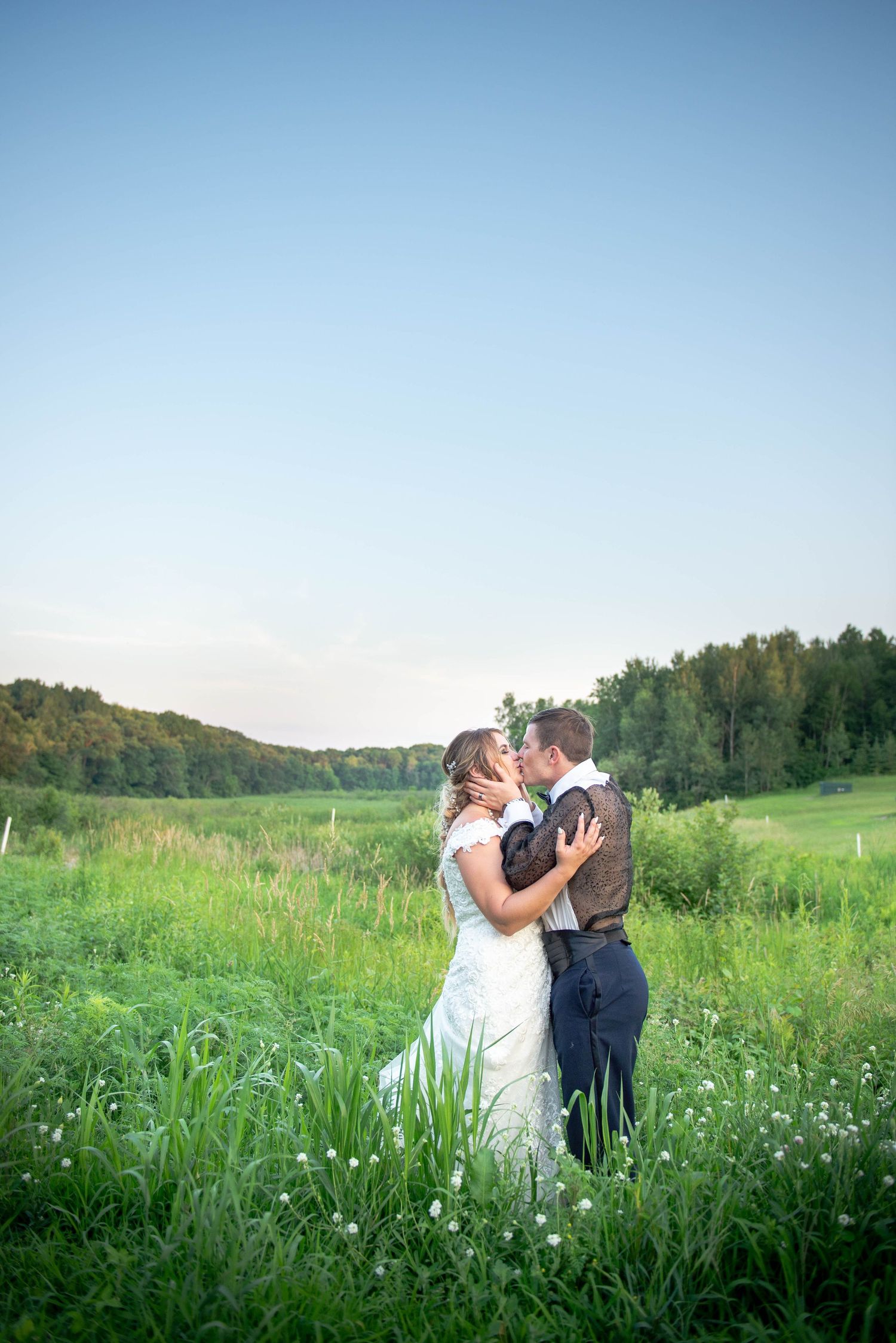 Newlywed couple shares intimate moment in sunny meadow with rolling hills and trees in background.  Zimmerman MN Weddings