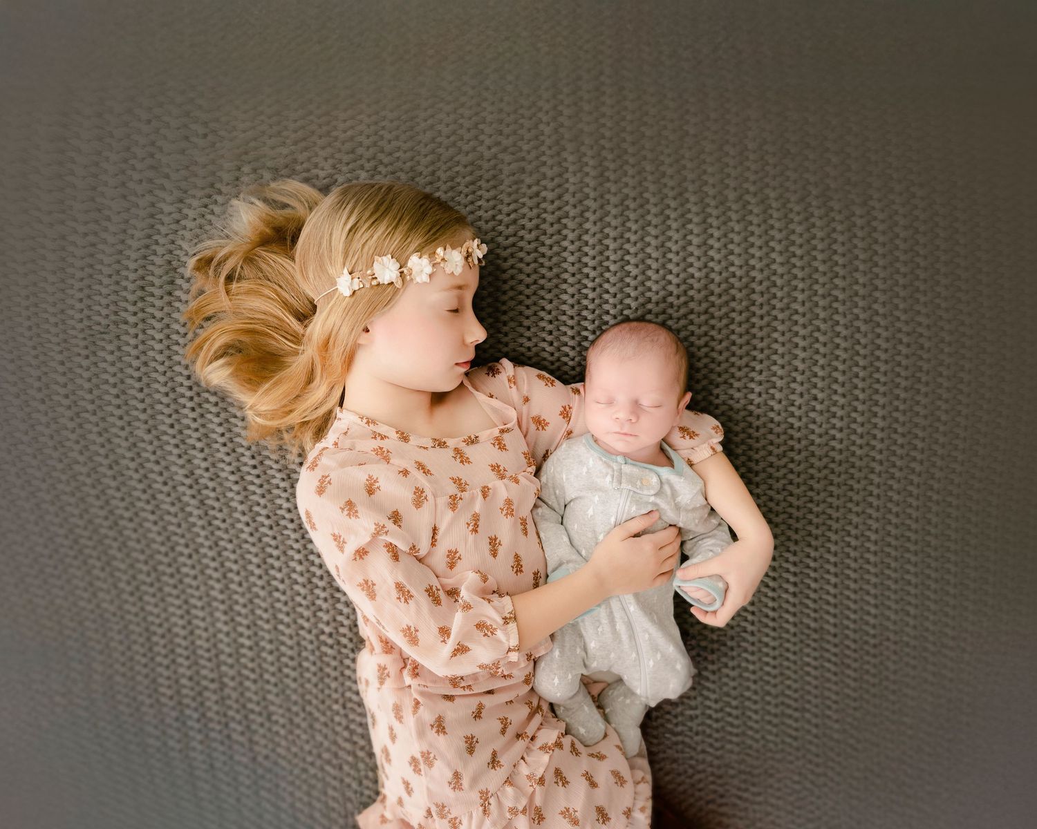 Minnesota Best newborn photos - A tender moment captured from above as two people lie on a gray textured surface in pink and white clothing.