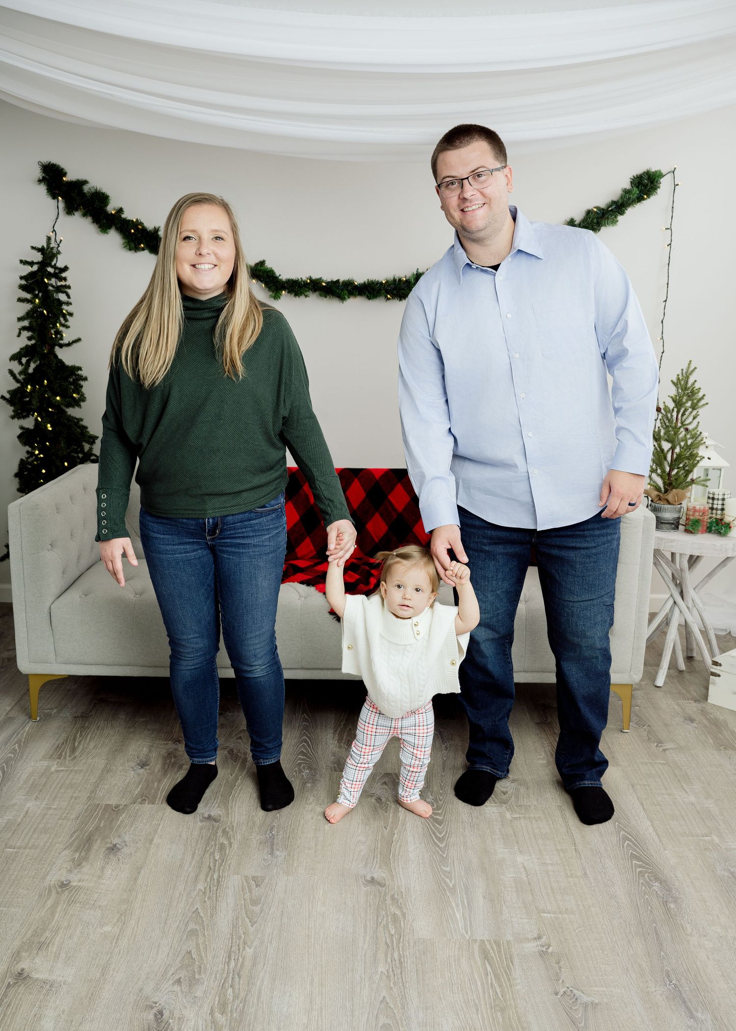 Family standing together in a white studio room decorated with Christmas trees and garland against a light floor.