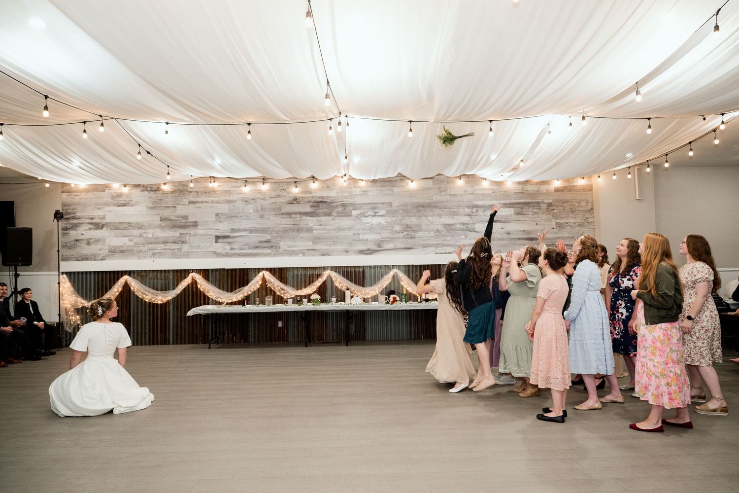 Wedding reception venue decorated with string lights and white fabric draping across ceiling.
