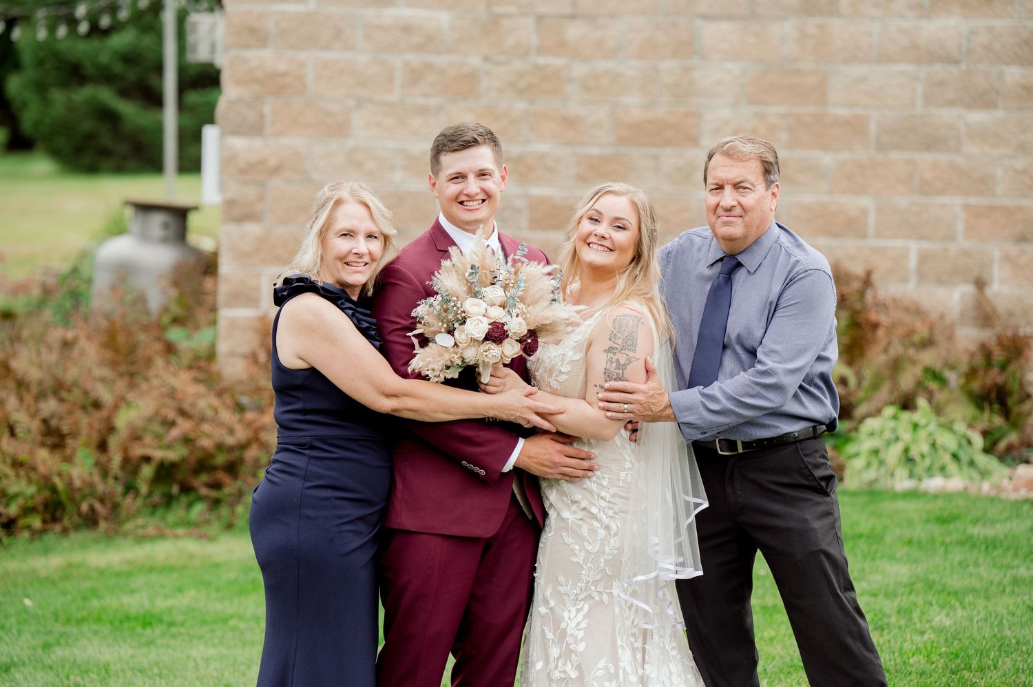 Family group embrace and smile while celebrating at outdoor wedding venue.