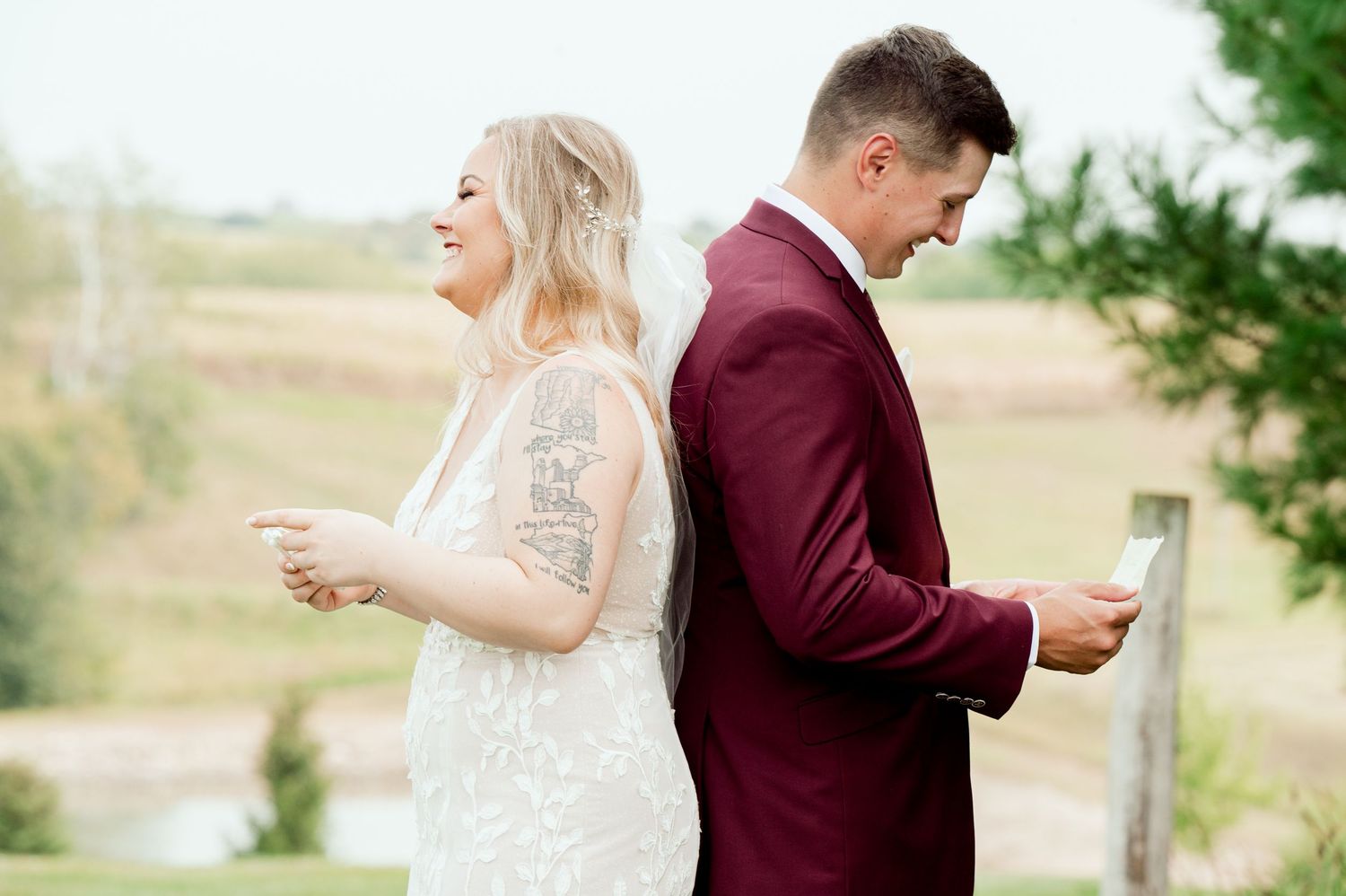 A bride and groom share a candid moment standing back to back while checking their phones in an outdoor setting.