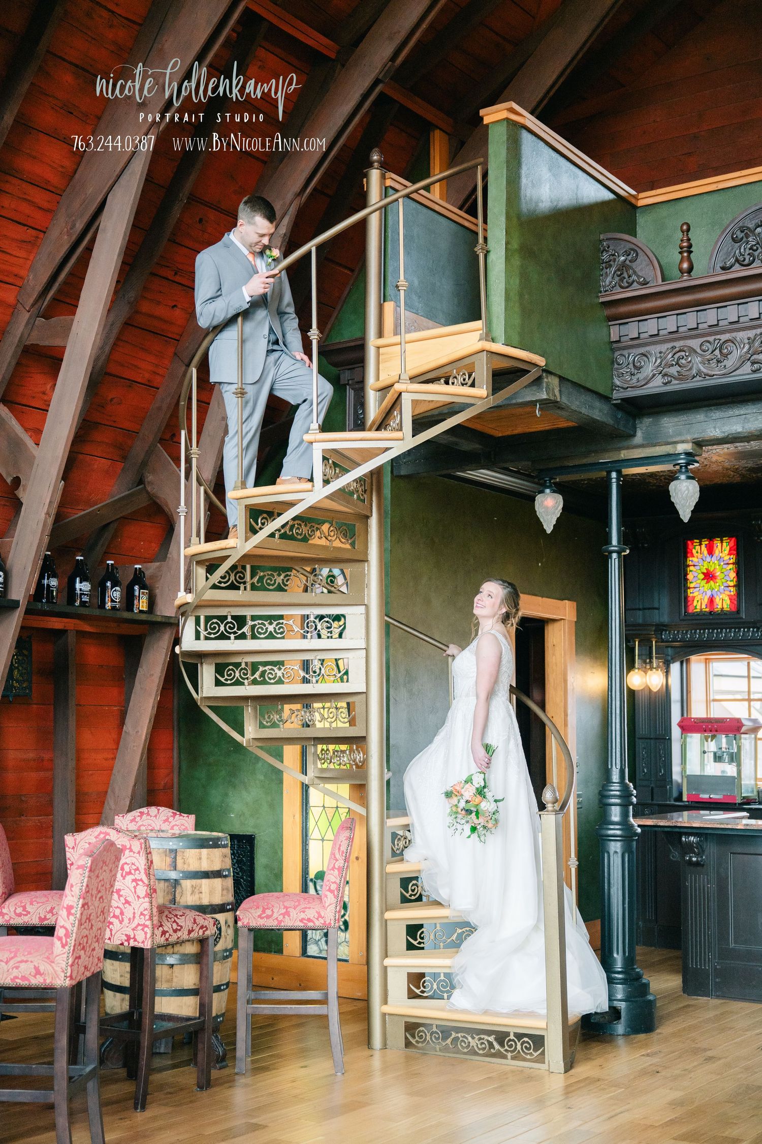 Bride in white gown and groom in gray suit on ornate spiral staircase in elegant rustic wedding venue. Crooked Willow Osakis