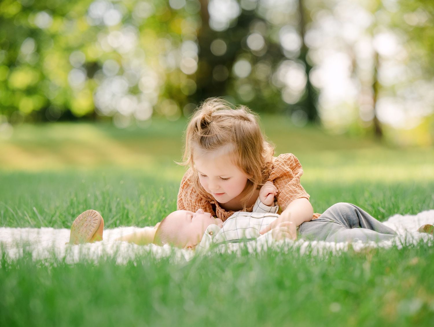 Young girl lying on white blanket outdoors on green grass in natural sunlight.. Minnesota milestone photographer