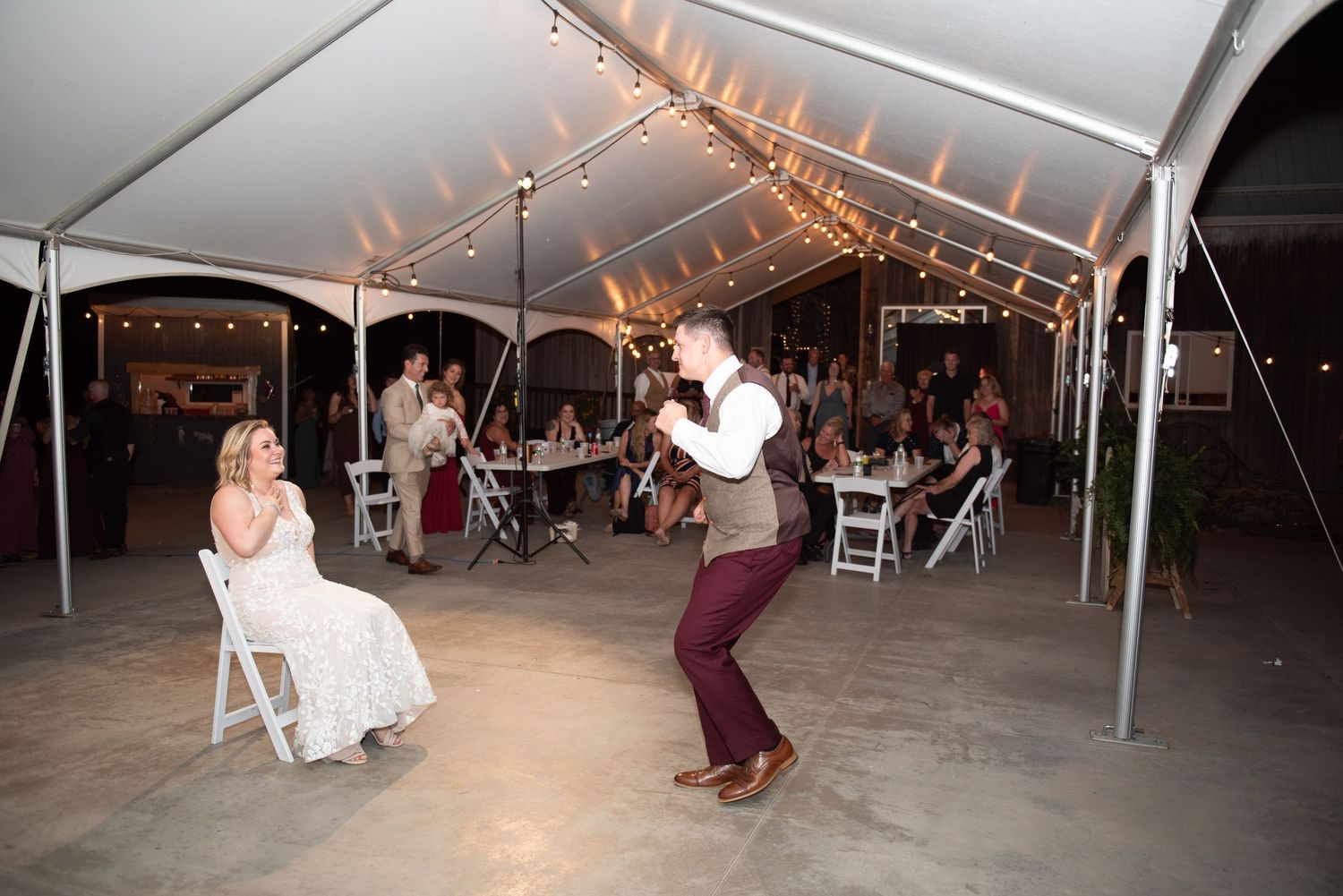 A wedding reception under a white tent with string lights and dancers on the dance floor during an evening celebration.