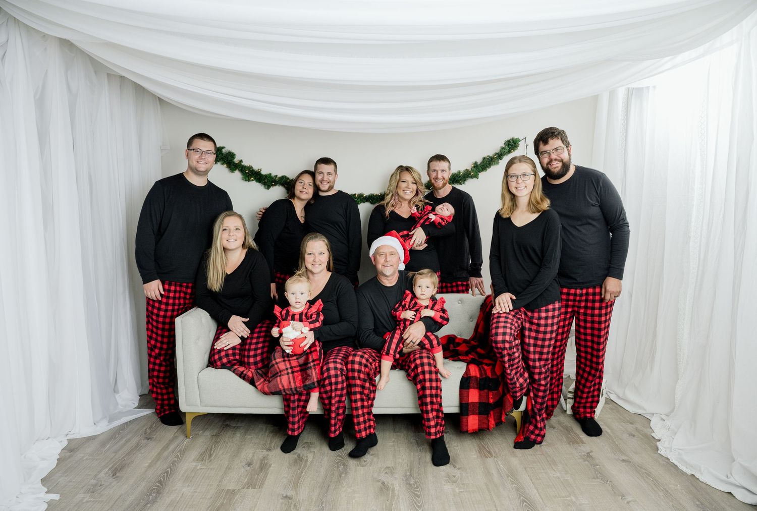 Group wearing coordinated red plaid and black outfits posing together on white backdrop during holiday photo session.