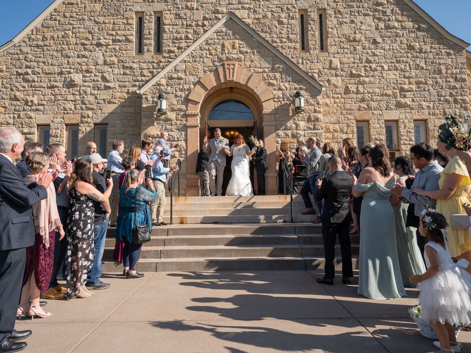 Wedding guests line the steps of a stone church as a bride and groom exit their ceremony.