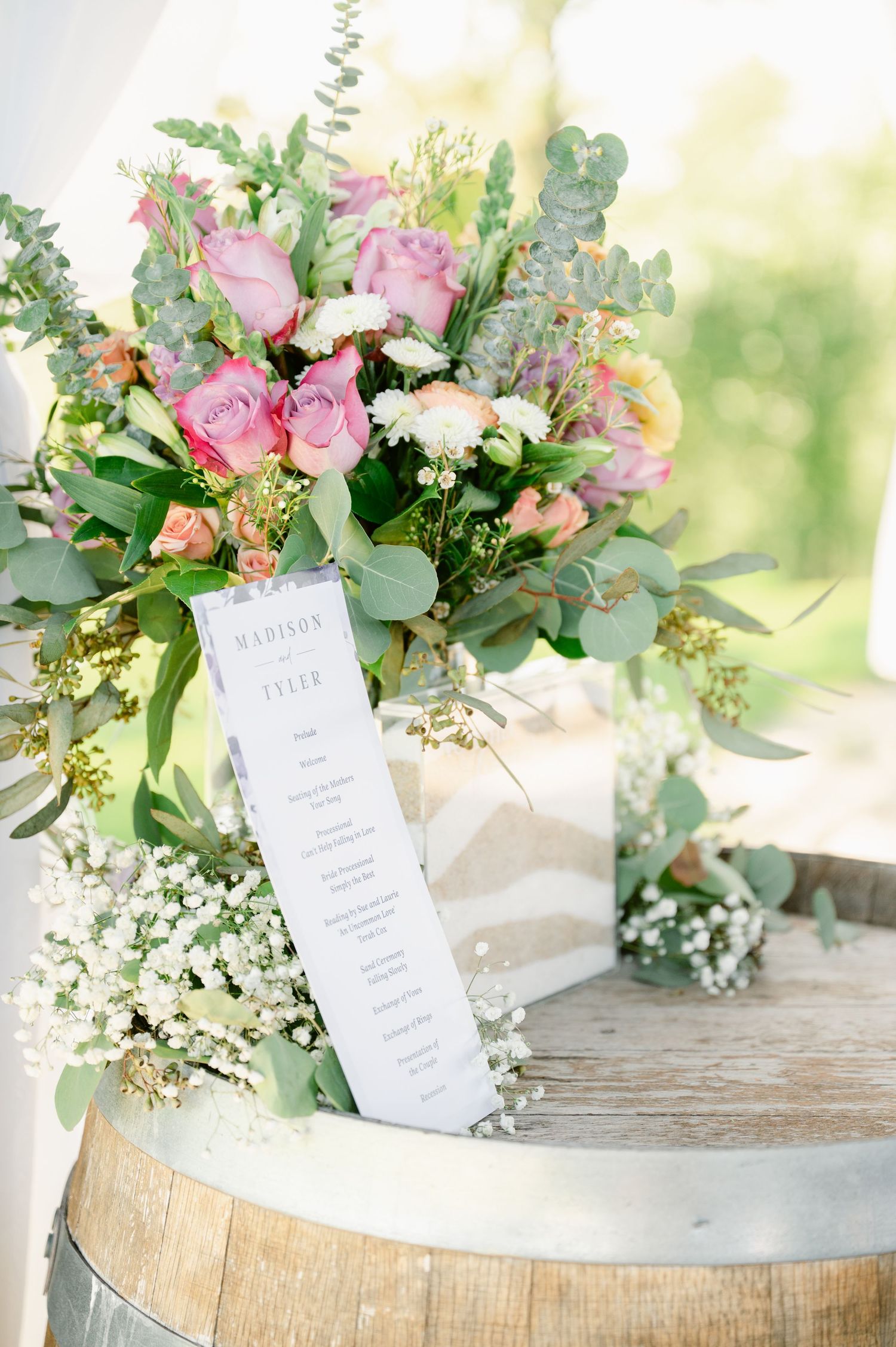 Central MN Wedding Photos - Elegant wedding seating chart displayed beside a lush pink and white floral bouquet on a rustic barrel.