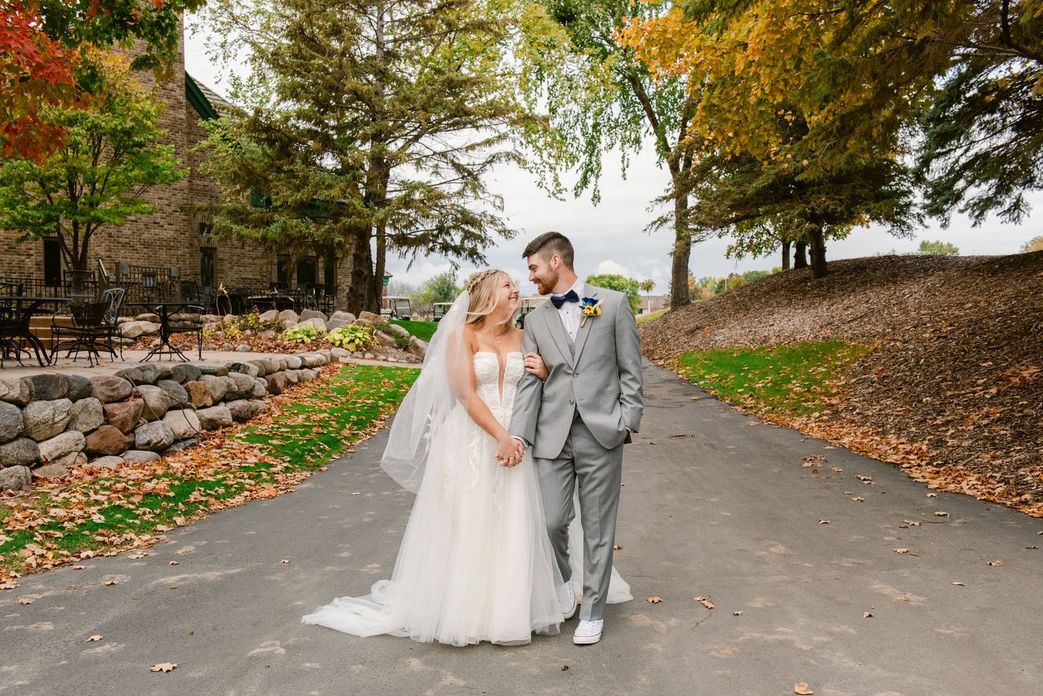 Central MN Wedding Photos | Bride and groom walking together on path surrounded by fall foliage.