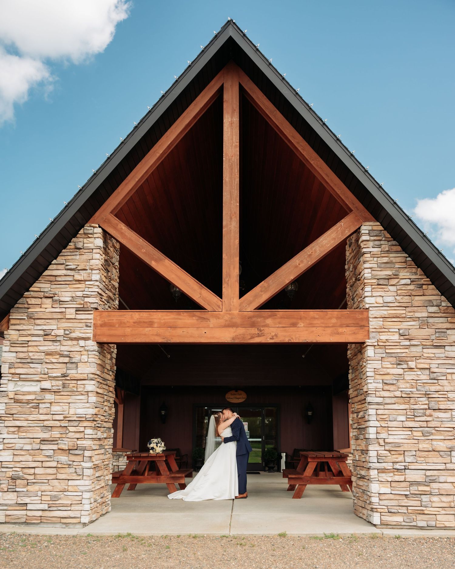A rustic stone and wood pavilion with multiple covered sections creates an elegant outdoor venue space at Northern Lights near Milaca MN.