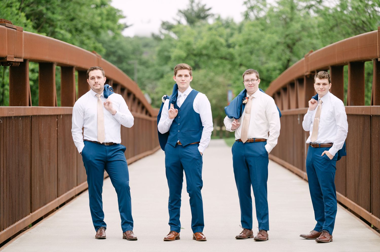 Wedding party in navy blue and white attire walking across a wooden bridge.