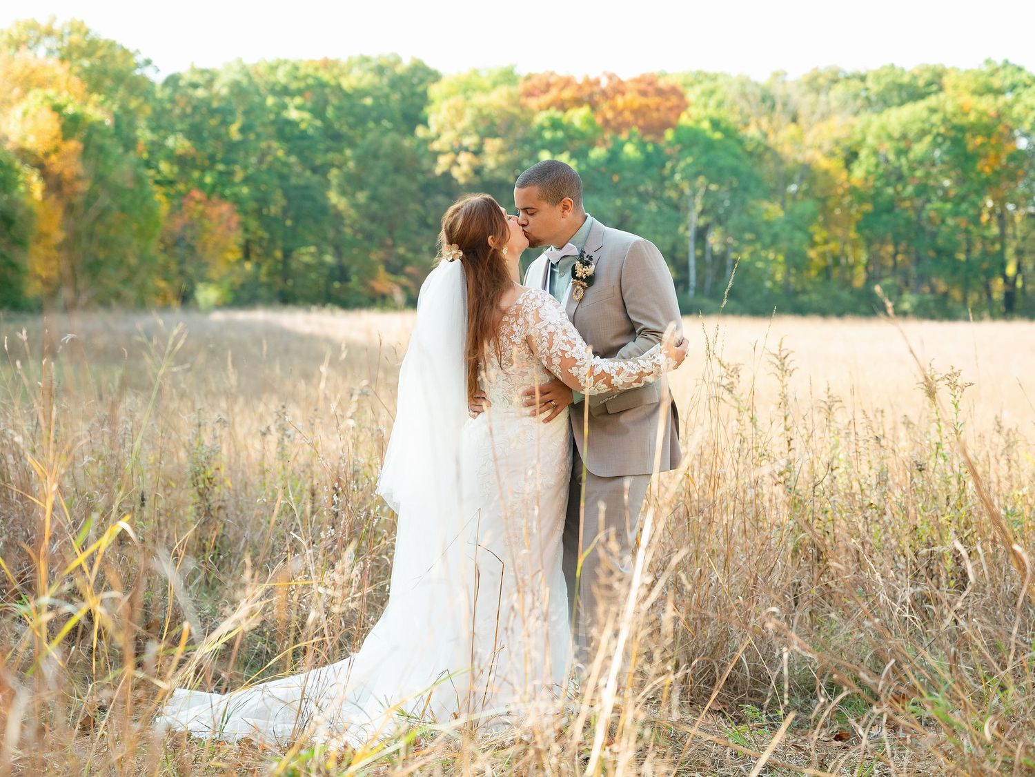 Newlyweds share tender moments together in a sunlit autumn field with golden grass and trees.