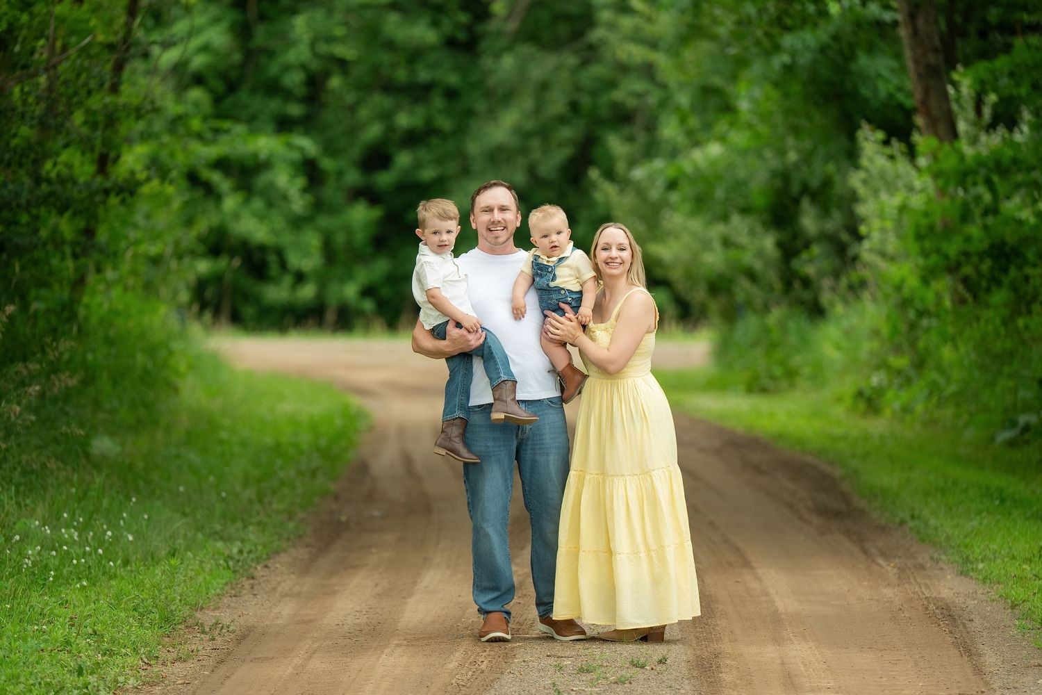People in casual and formal attire standing together on a dirt path surrounded by lush green foliage in nature. Family Portraits & Milestone